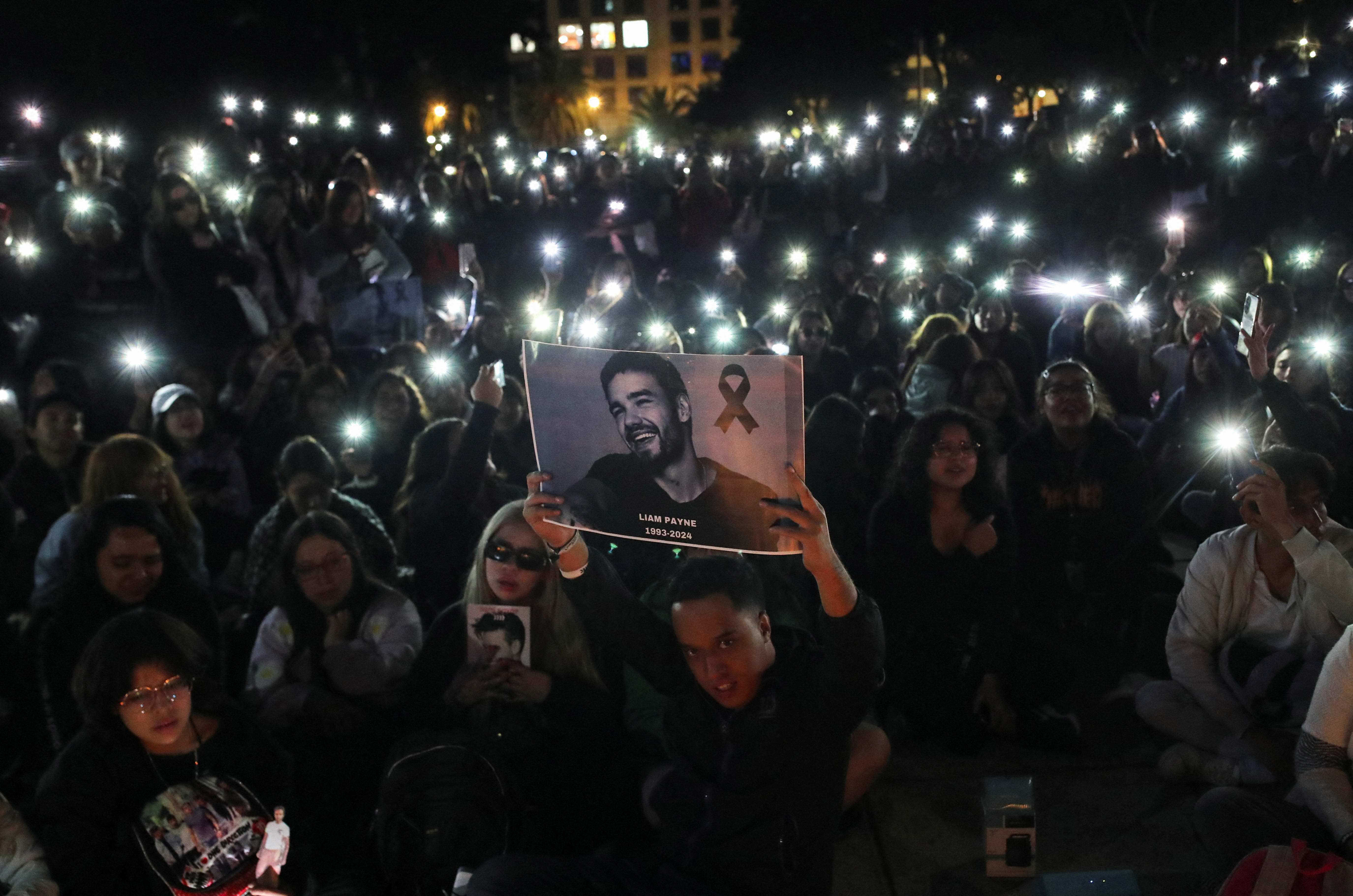 A man holds a poster with an image of Liam Payne next to One Direction fans as they gather to pay tribute to Liam Payne, at the Monument of the Revolution, in Mexico City, Mexico October 17, 2024. REUTERS/Henry Romero