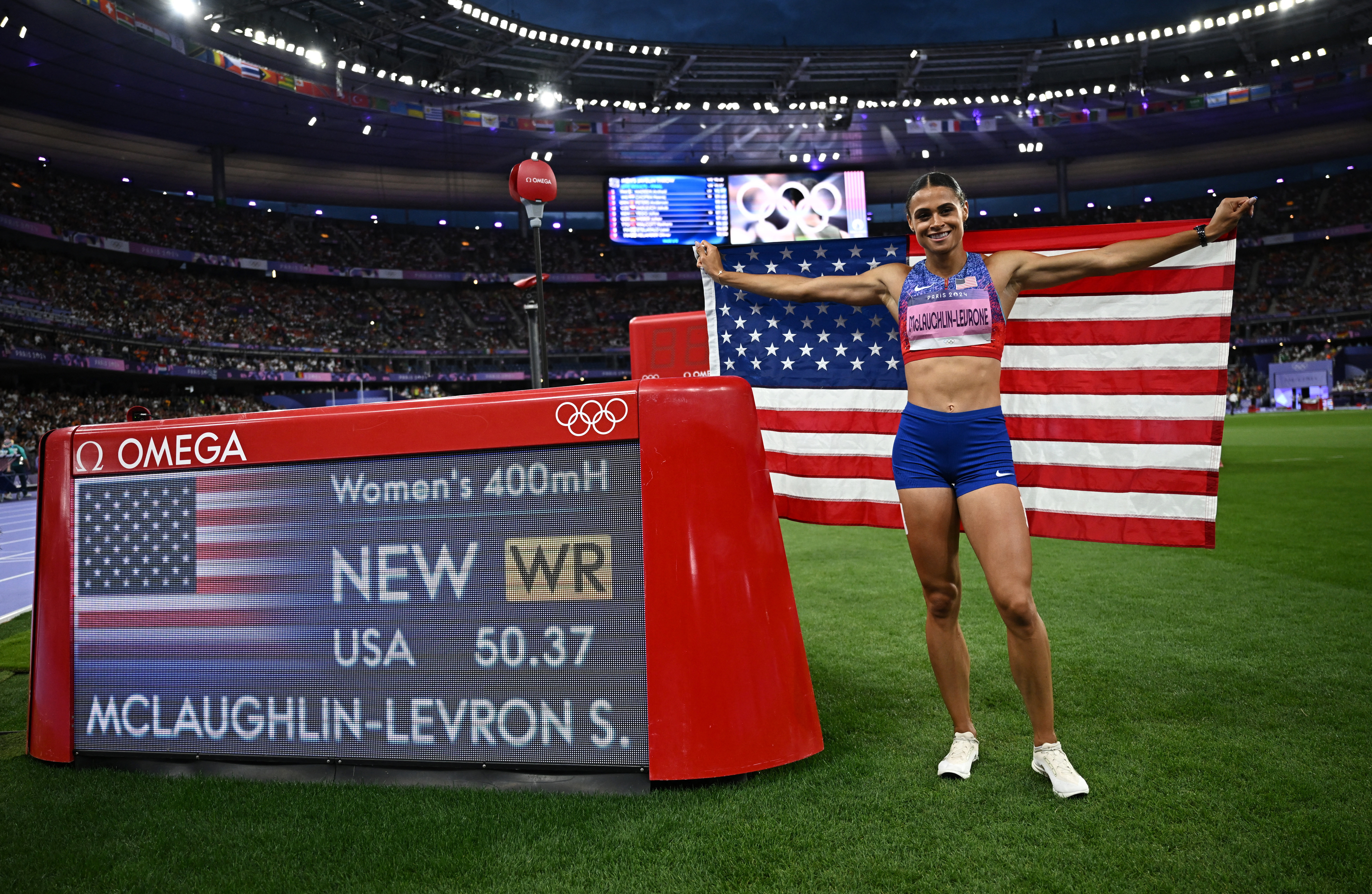 Paris 2024 Olympics - Athletics - Women's 400m Hurdles Final - Stade de France, Saint-Denis, France - August 08, 2024. Sydney McLaughlin-Levrone of United States celebrates with her national flag after winning gold and a new world record. REUTERS/Dylan Martinez