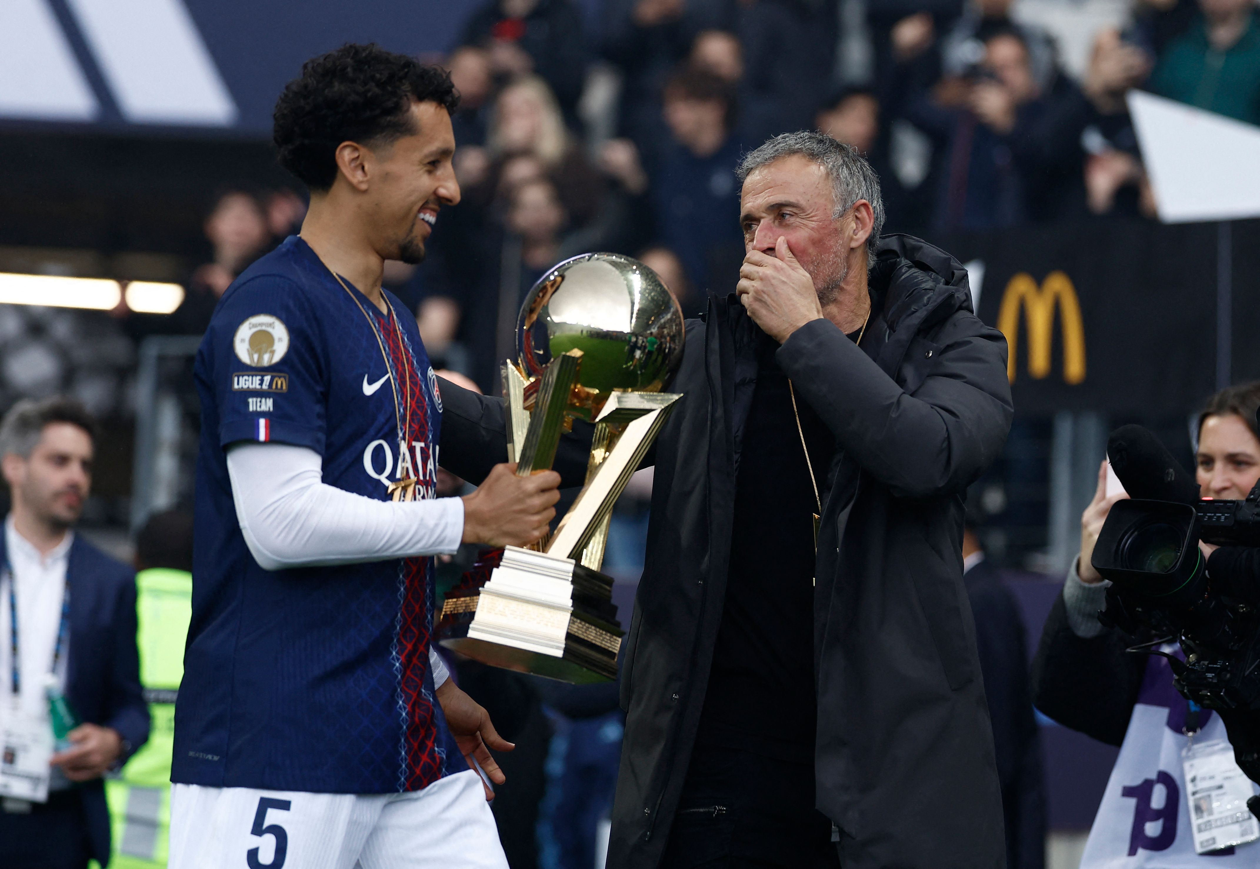 Paris Saint-Germain's Brazilian defender #05 Marquinhos (L) and Paris Saint-Germain's Spanish head coach Luis Enrique (R) celebrate with the French Ligue 1 trophy after winning the championship ahead of the French L1 football match between Paris FC and Paris Saint-Germain (PSG) at the Stade Jean-Bouin in Paris on May 17, 2026. (Photo by Kenzo TRIBOUILLARD / AFP)