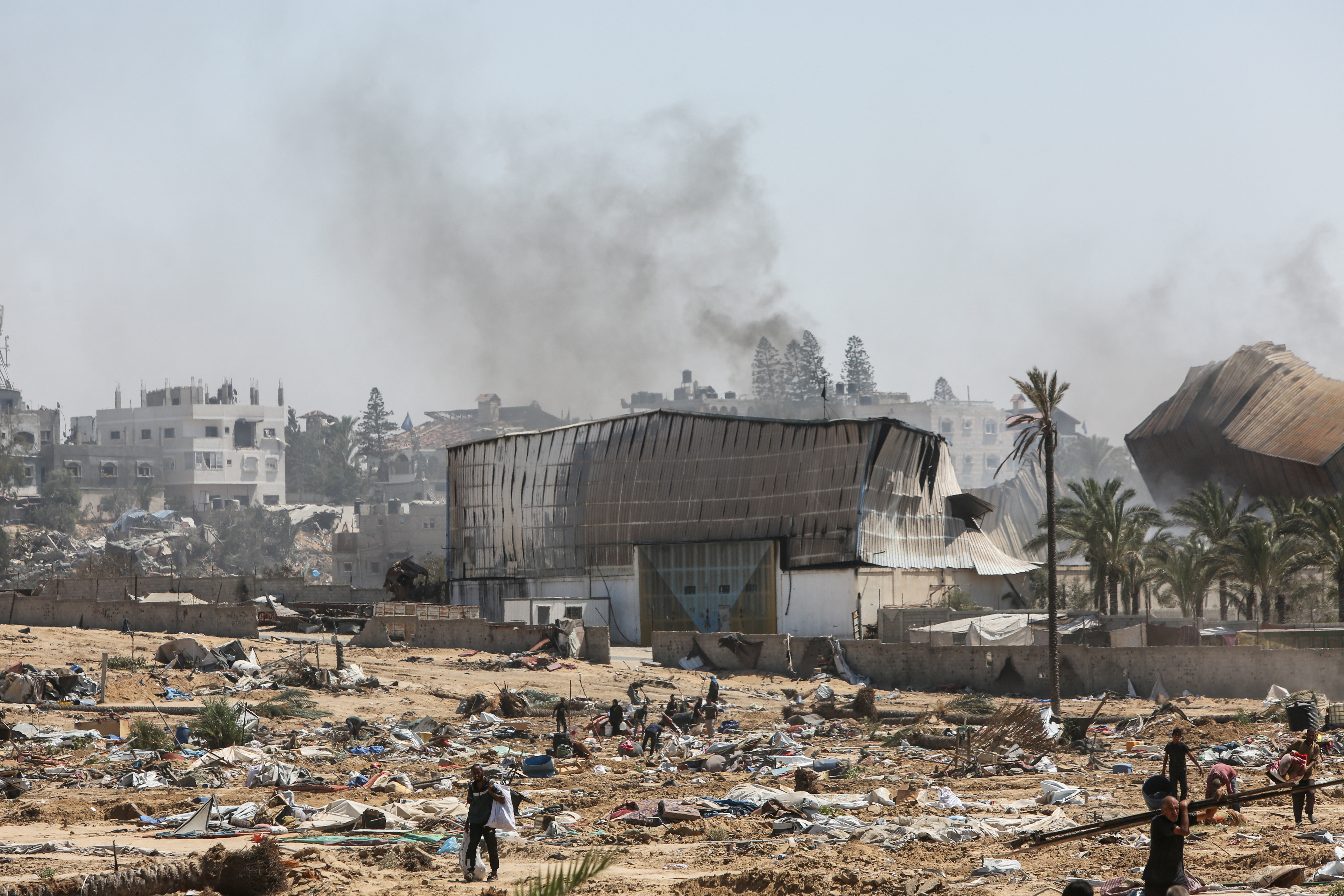 Smoke rises as displaced Palestinian walk with their belongings in the aftermath of an Israeli military operation in Deir Al-Balah, in the central Gaza Strip, July 22, 2025. REUTERS/Hatem Khaled