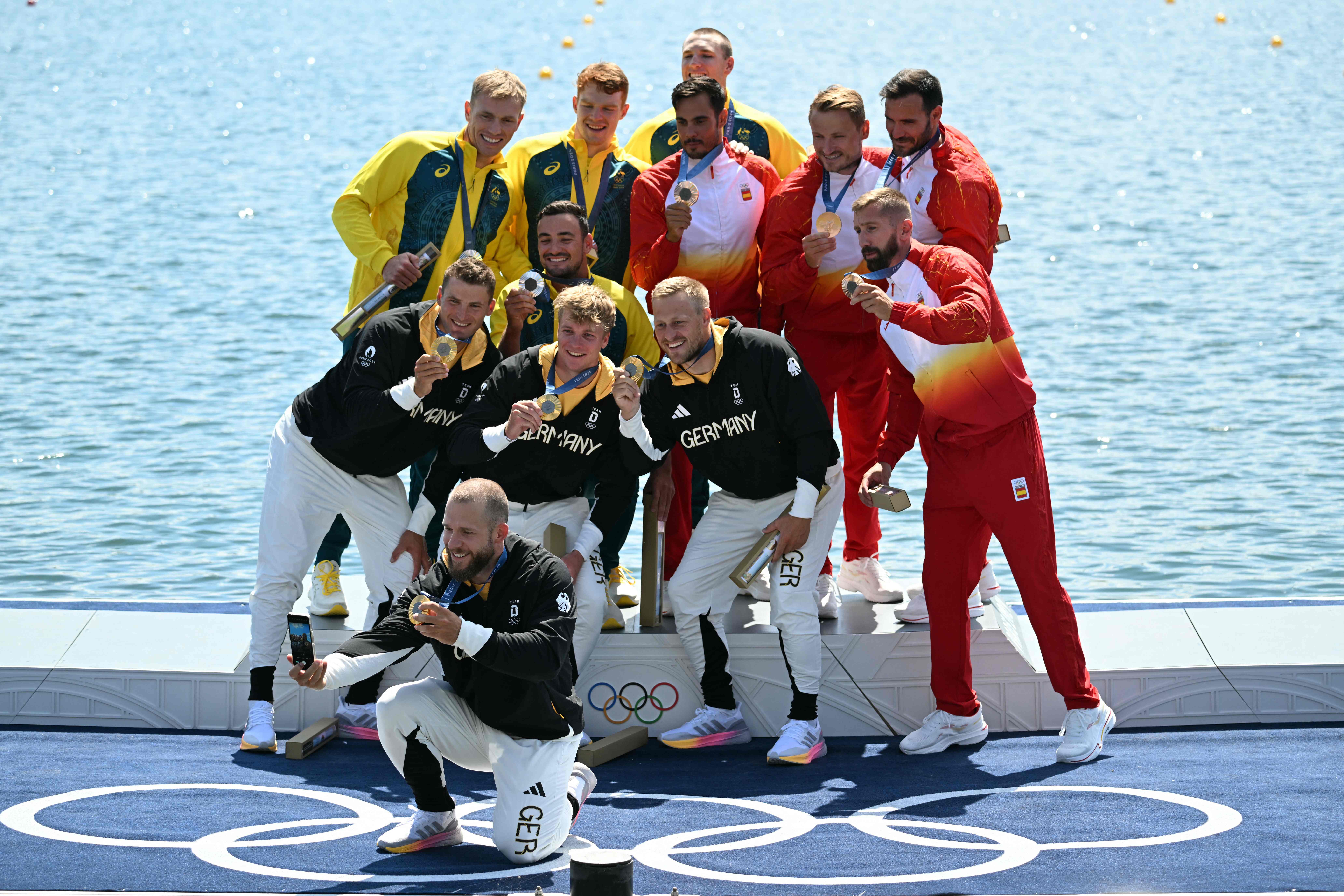 Australia's silver medallists (TOP L) Riley Fitzsimmons, Pierre Van Der Westhuyzen, Jackson Collins and Noah Havard, Germany's gold medallists (BOTTOM L) Max Rendschmidt, Max Lemke, Jacob Schopf and Tom Liebscher-Lucz, and Spain's bronze medallists (R) Rodrigo Germade, Saul Craviotto, Carlos Arevalo and Marcus Cooper pose for a selfie photo on the podium during the medal ceremony following the men's kayak four 500m final of the canoe sprint competition at Vaires-sur-Marne Nautical Stadium in Vaires-sur-Marne during the Paris 2024 Olympic Games on August 8, 2024. (Photo by Bertrand GUAY / AFP)