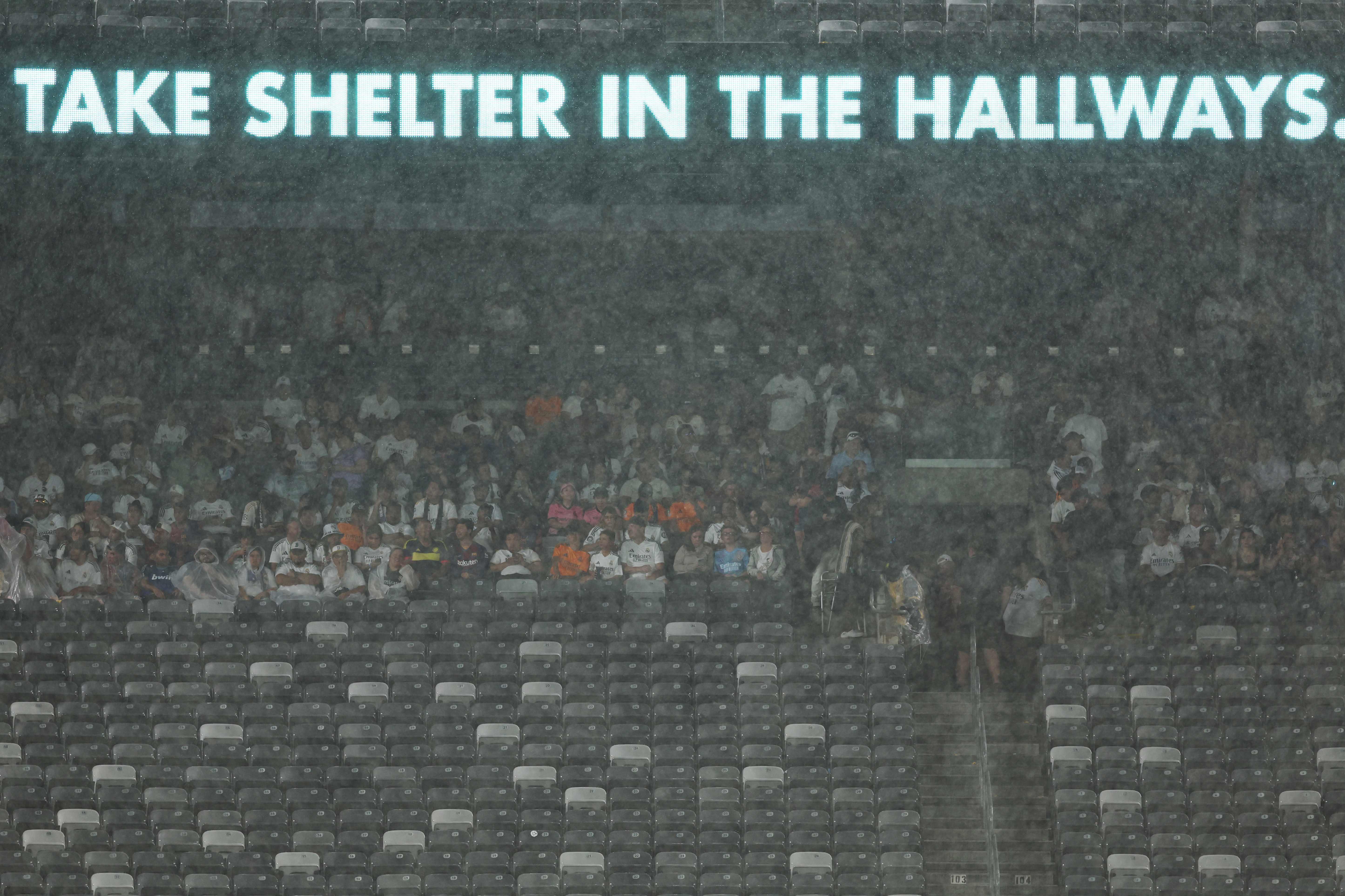 Spectators shelter from rain as the match has been suspended during the pre-season club friendly football match between Real Madrid and FC Barcelona at MetLife Stadium, in East Rutherford, New Jersey on August 3, 2024. (Photo by Charly TRIBALLEAU / AFP)