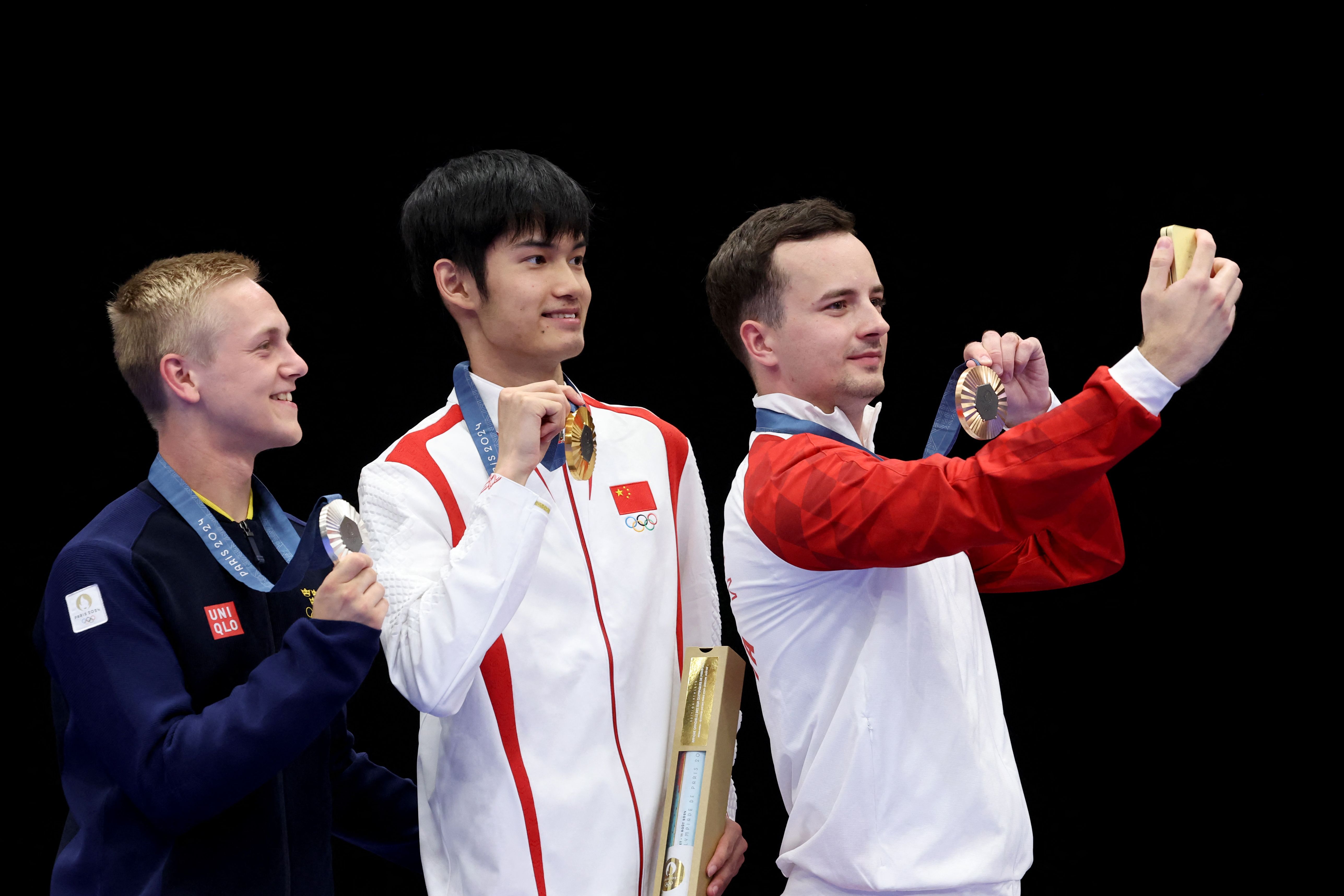 (FromL) Silver medalist, Sweden's Victor Lindgren, gold medalist China's Sheng Lihao and bronze medalist Croatia's Miran Maricic take a selfie on the podium at the end of the shooting 10m air rifle men's final during the Paris 2024 Olympic Games at Chateauroux Shooting Centre on July 29, 2024. (Photo by ALAIN JOCARD / AFP)