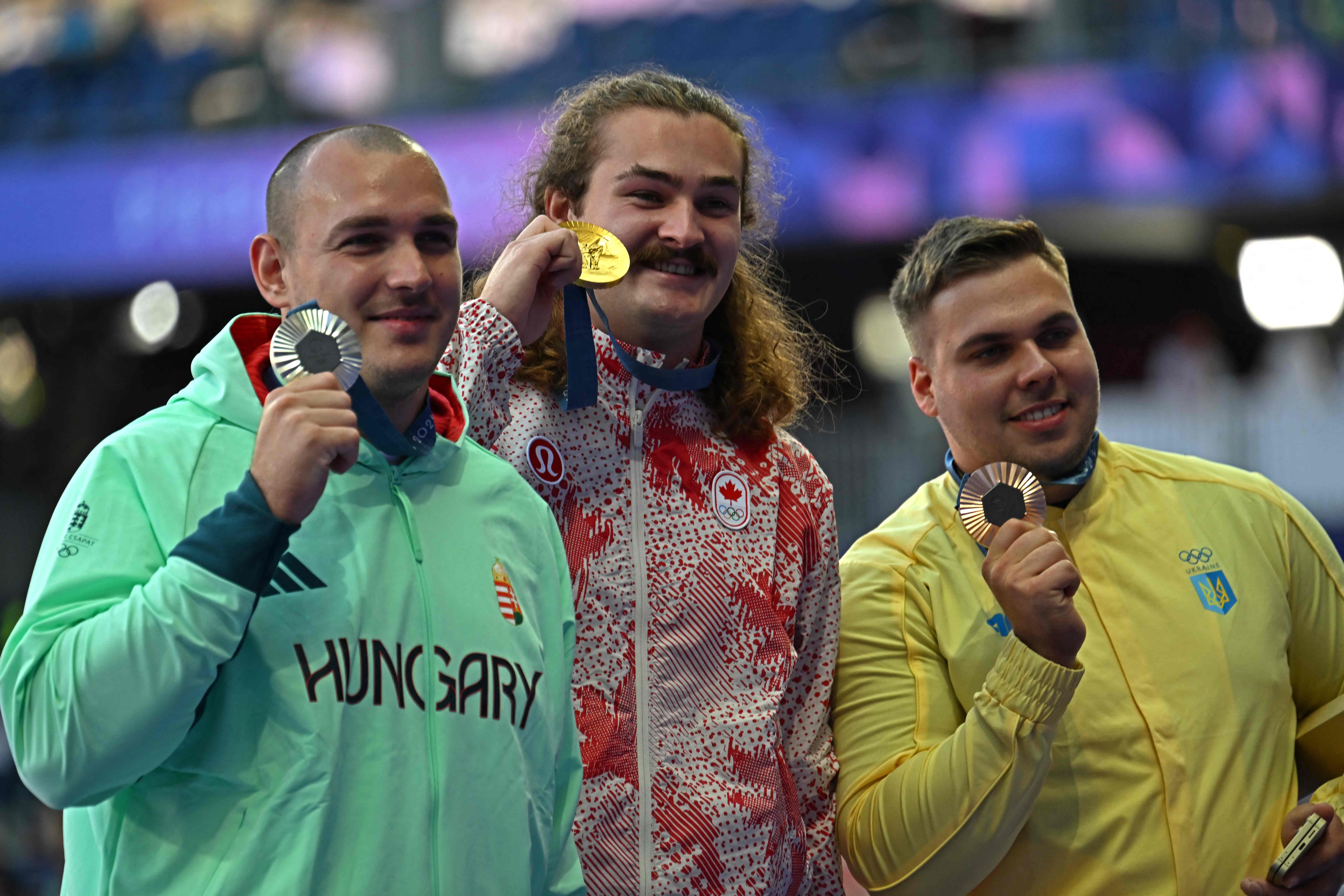 Silver medallist Hungary's Bence Halasz (L), gold medallist Canada's Ethan Katzberg (C) and bronze medallist Ukraine's Mykhaylo Kokhan celebrate on the podium during the victory ceremony for the men's hammer throw athletics event during the Paris 2024 Olympic Games at Stade de France in Saint-Denis, north of Paris, on August 5, 2024. (Photo by MARTIN BERNETTI / AFP)