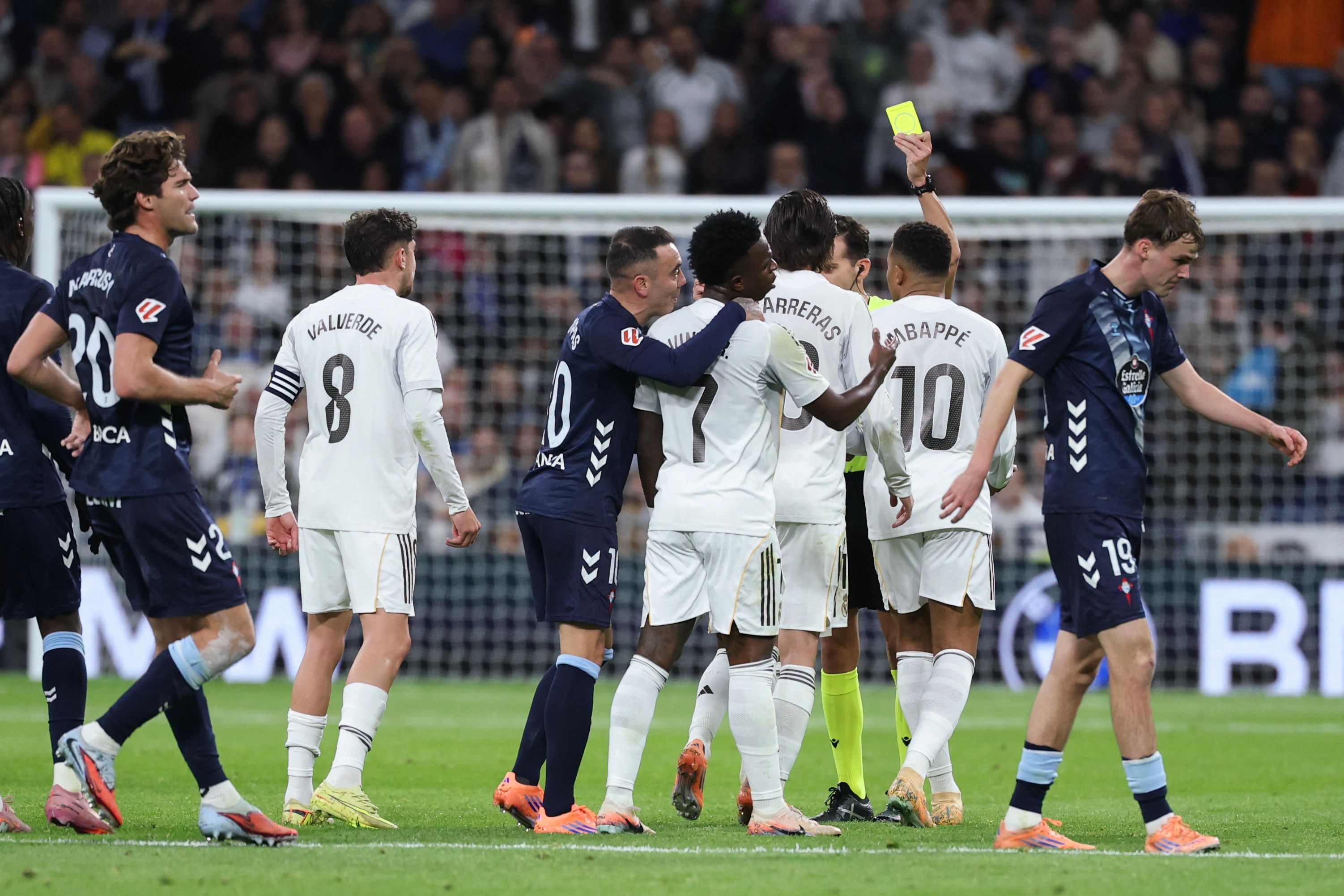 Referee Alejandro Quintero holds up a yellow card as players argue during the Spanish league football match between Real Madrid CF and RC Celta de Vigo at the Santiago Bernabeu Stadium in Madrid on December 7, 2025. (Photo by Thomas COEX / AFP)