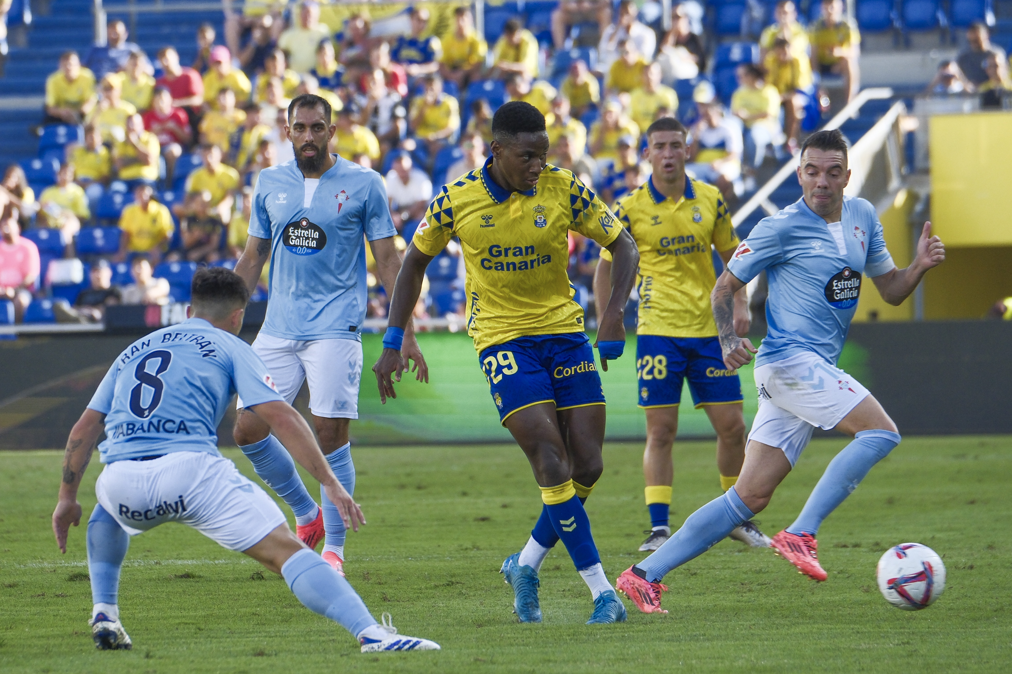 LAS PALMAS DE GRAN CANARIA, 05/10/2024.- El centrocampista de la UD Las Palmas Dário Essugo (c) centra el balón junto a Iago Aspas (d), del Celta, durante el encuentro de la jornada 9 de LaLiga que UD Las Palmas y Celta de Vigo disputan este sábado en el estadio de Gran Canaria. EFE/Angel Medina G.
