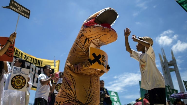 A Manille, le 8 septembre 2018, un manifestant habillé en dinosaure tient une pancarte "Go Fossil-free" ("Finissons-en avec les énergies fossiles"), au cours d'une manifestation dans le cadre de la journée mondiale "Rise for Climate" (Debout pour le climat).
