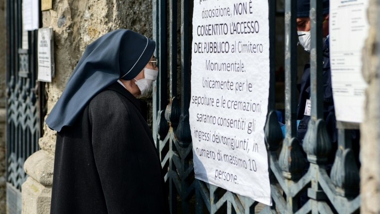 Une religieuse devant la porte d'entrée du cimetière Monumental de Bergame, fermé, le 20 mars 2020.
