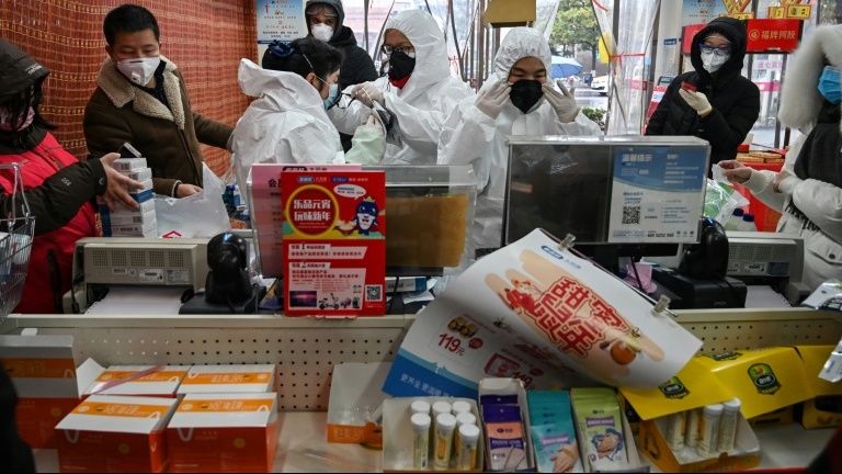 Du personnel médical, en combinaison et masque de protection, servent des clients dans une pharmacie de Wuhan, le 25 janvier 2020 en Chine.
