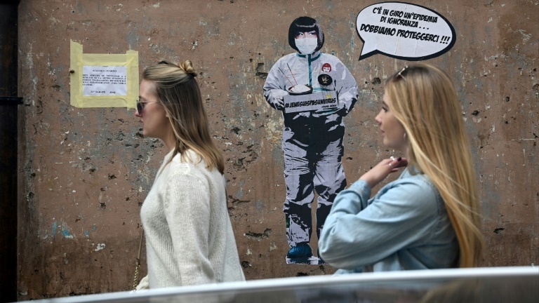 Deux femmes passent devant un message mural où il est écrit: "Il y a une épidémie d'ignorance dans l'air, nous devons nous protéger", par l'artiste Laika, près du quartier chinois de Rome, le 4 février 2020.
