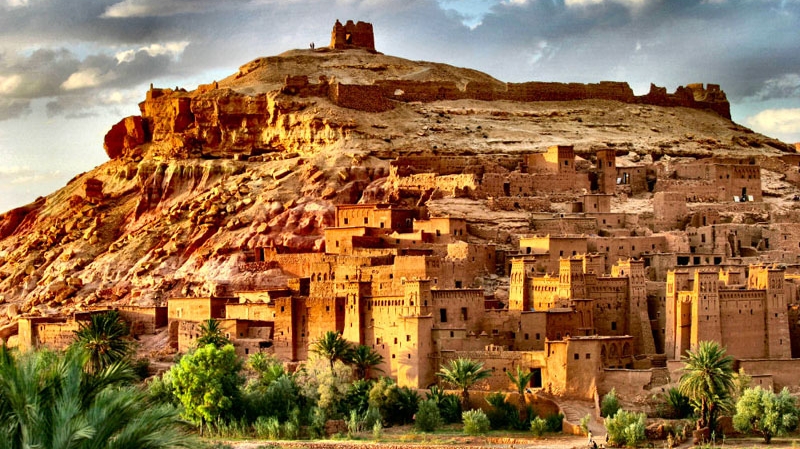 Situé à 30 km d’Ouarzazate, le village d’Aït-Benhaddou offre un spectacle architectural de strates rocheuses. L’endroit se présente comme un ensemble de bâtiments de terre entourés de murailles. 
