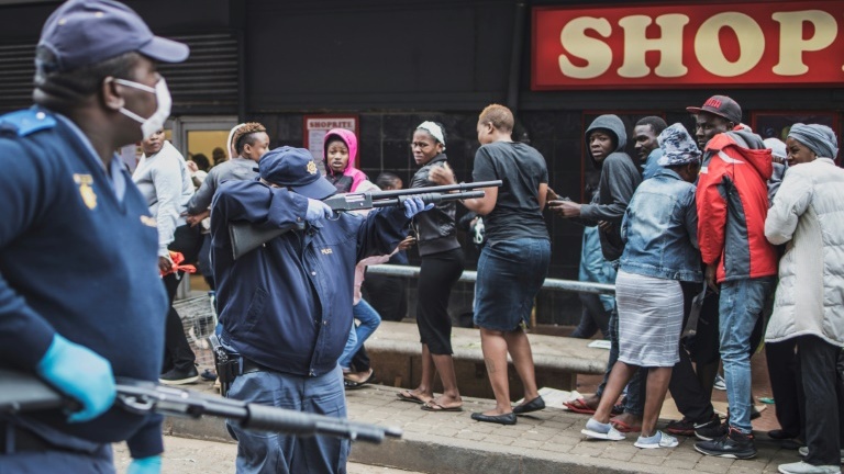 Un policier sud-africain pointe son fusil à balles en caoutchouc sur la foule pour faire respecter les consignes de distance sociale devant un supermarché de Johannesburg, le 28 mars 2020, pendant le confinement instauré pour lutter contre l'épidémie du nouveau coronavirus.
