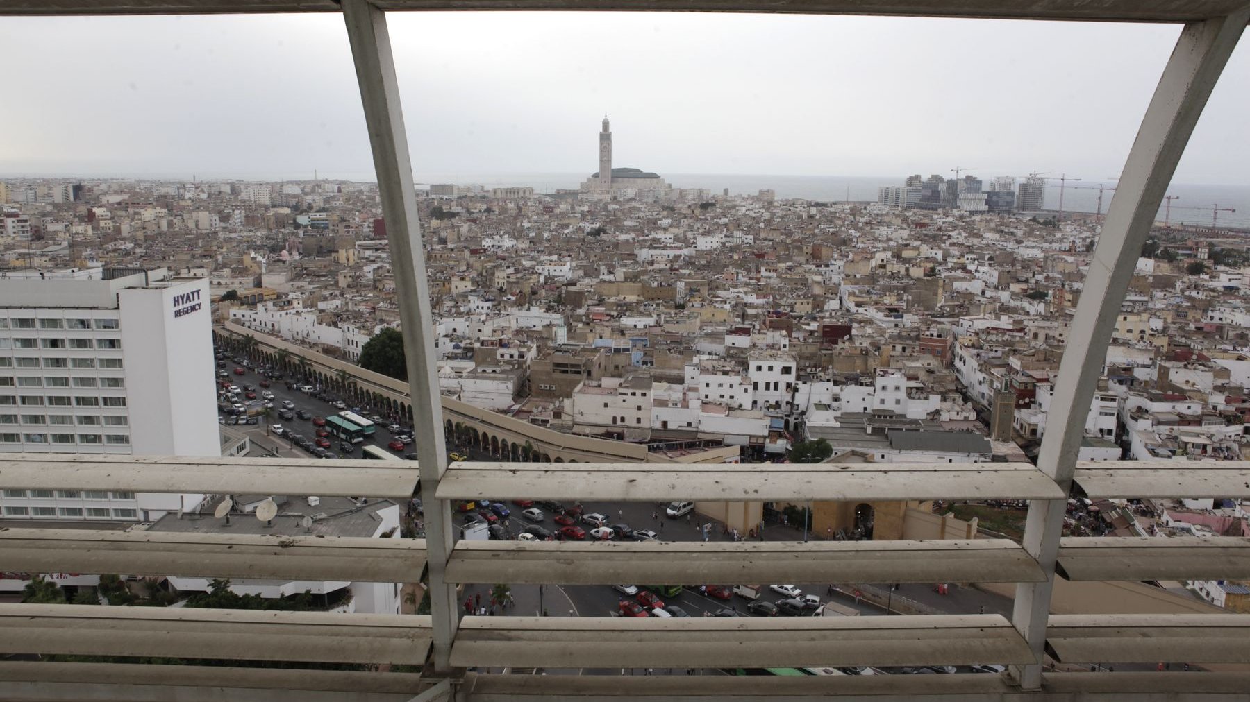 Une vue panoramique de Casablanca. Bâtiments luxueux et amas de petits carrés de sucre encastrés et chaotiquement amalgamés. Déferlentes de voitures. Vue d'en haut, coupée de ses bruits, la ville offre un spectacle surréaliste.  
