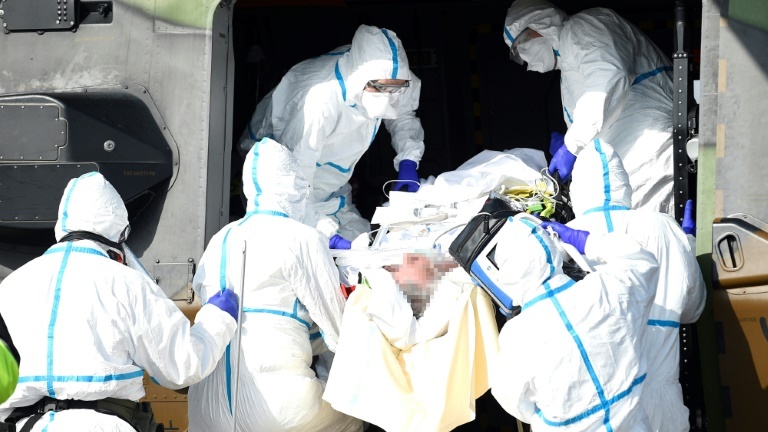 Des équipes médicales transportent un patient contaminé par le Covid-19 pour l'évacuer à bord d'un hélicoptère vers l'hôpital d'Essen, en Allemagne, le 28 mars 2020 sur un parking près du CHR de Metz.
