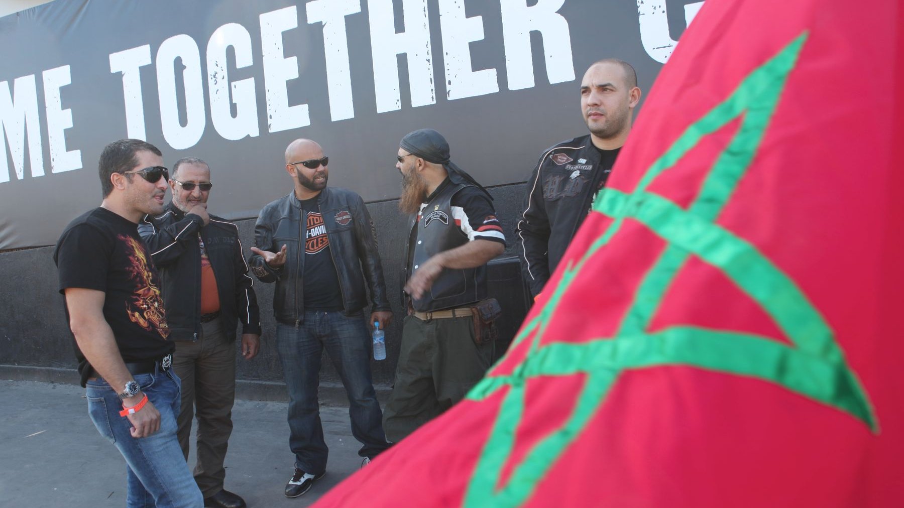 Petit attroupement de motard, derrière le drapeau marocain remué par les vents.
