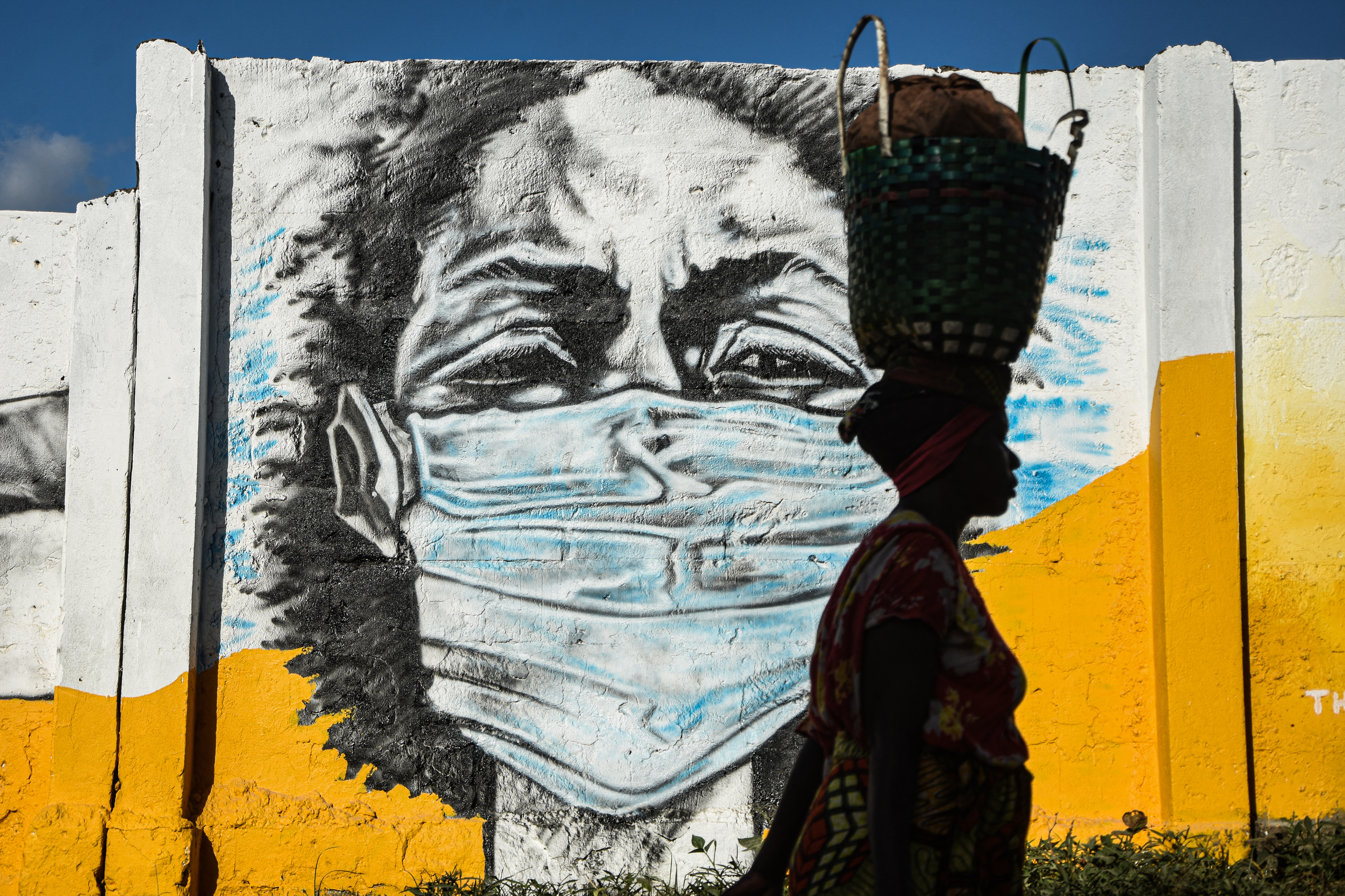 Une Tanzanienne marche devant un graffiti peint par le groupe d'artistes Wachata pour sensibiliser au port du masque à Dar es Salaam le 26 mai 2020.