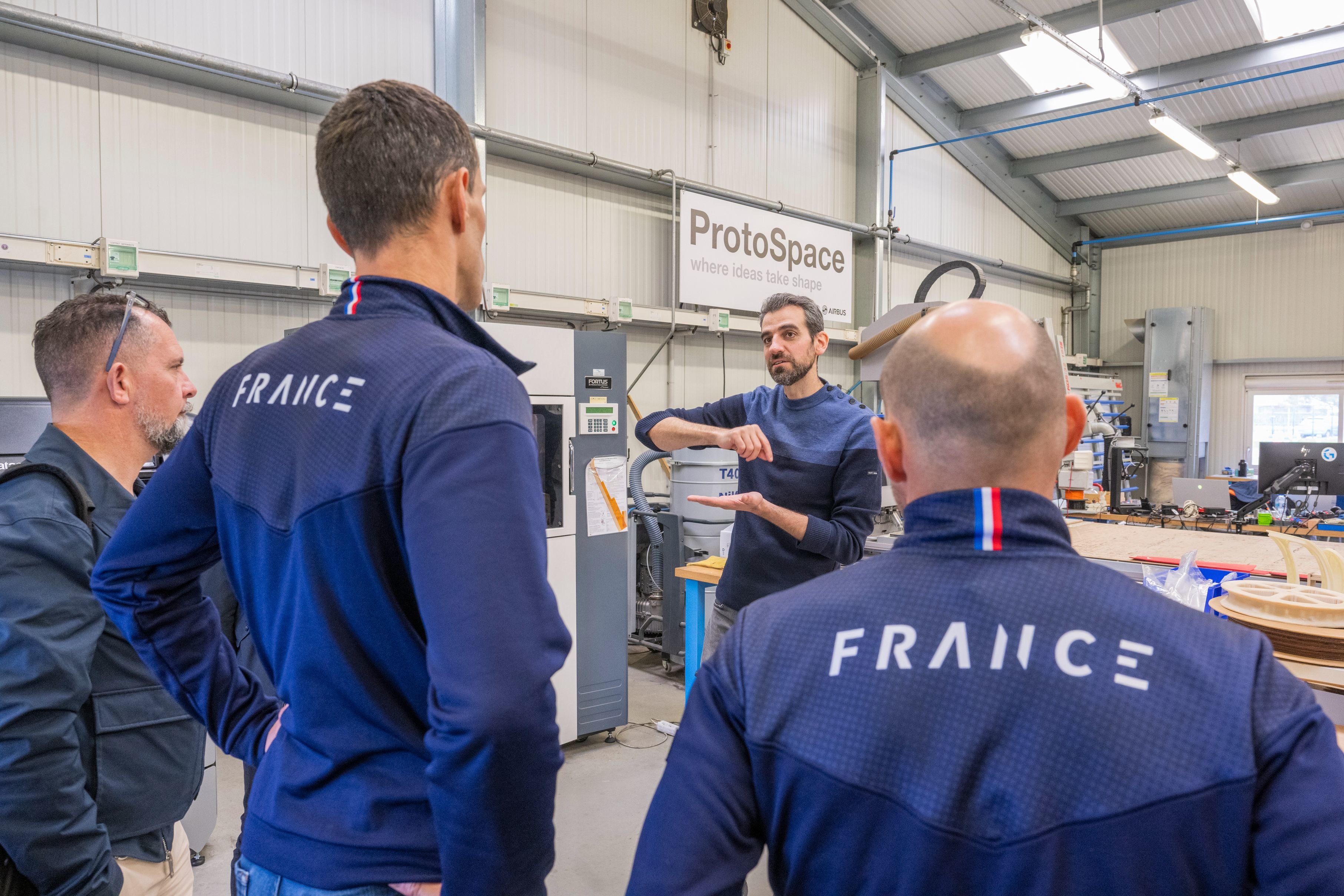 Christophe Debard (de face) responsable du labo ProtoSpace chez Airbus explique à Alexis Hanquinquant, para-triathlète (de dos au centre), les améliorations qu'il va apporter à sa lame. DR/Airbus