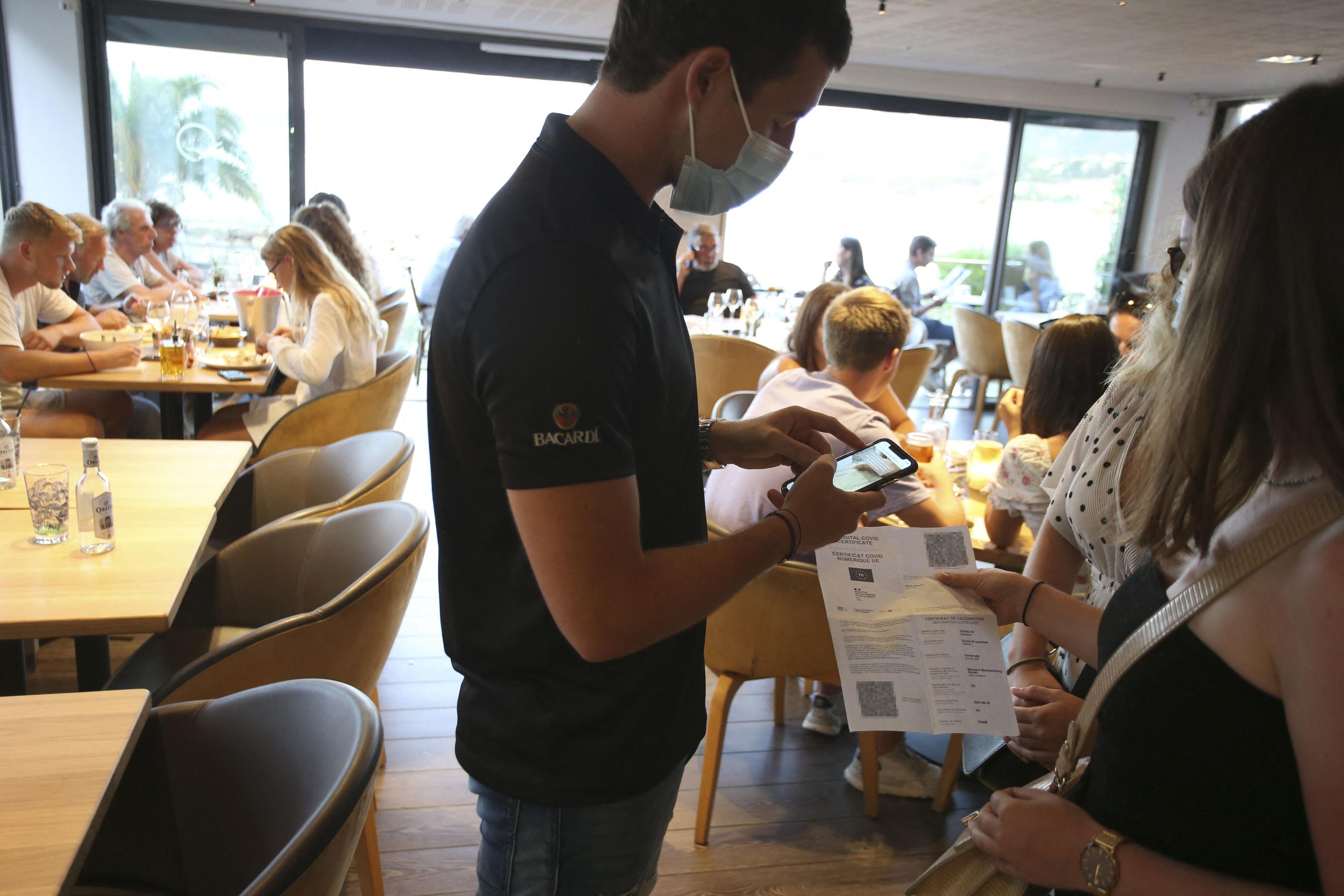 Le propriétaire d'un restaurant vérifie les pass sanitaires de clients en Corse. AFP/ Pascal Pochard-Casabianca