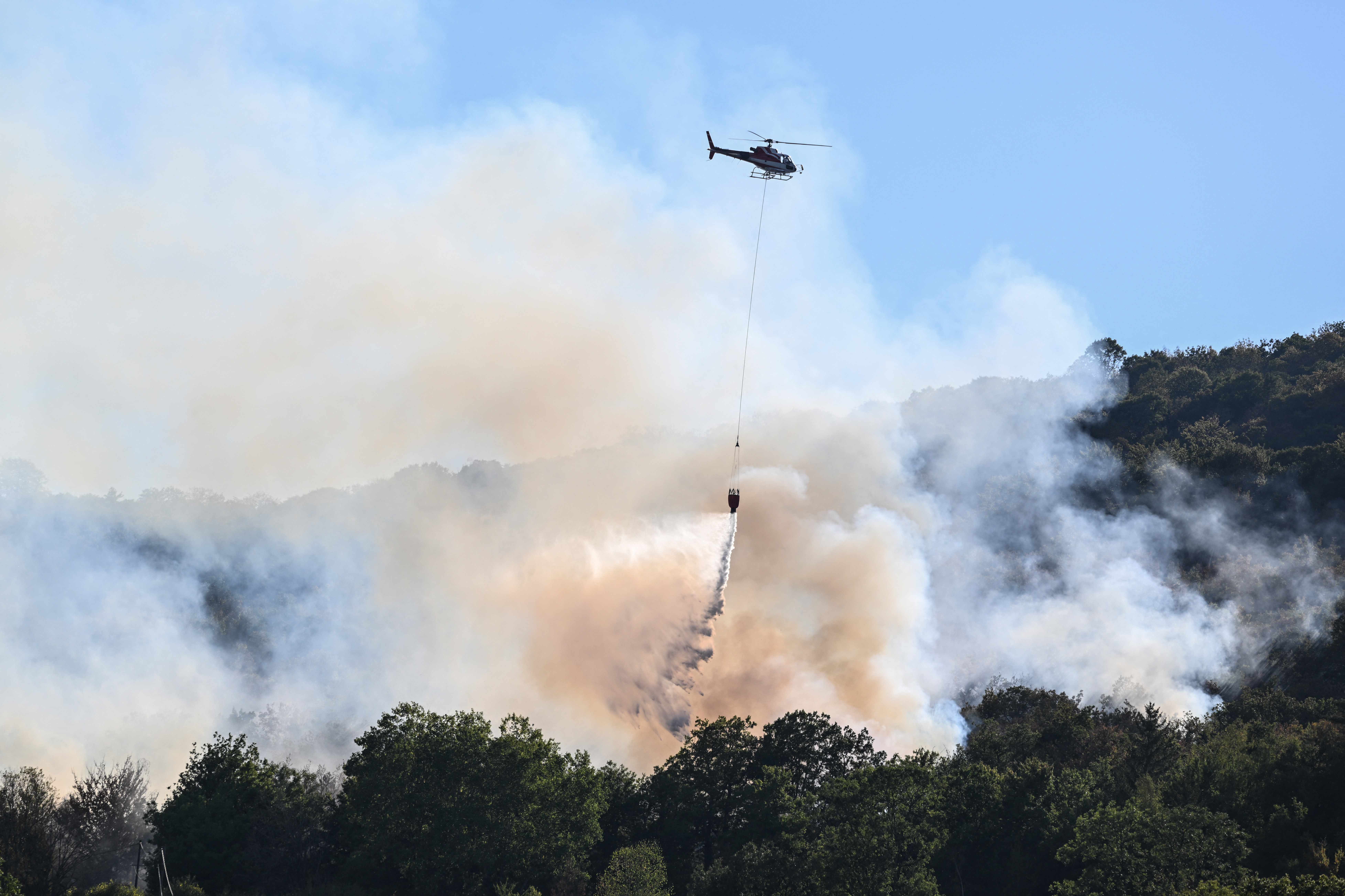 Un hélicoptère largue de l'eau sur des arbres lors d'un incendie près de Cernon, dans le Jura, le 11 août 2022. AFP/Jean-Philippe Ksiazek