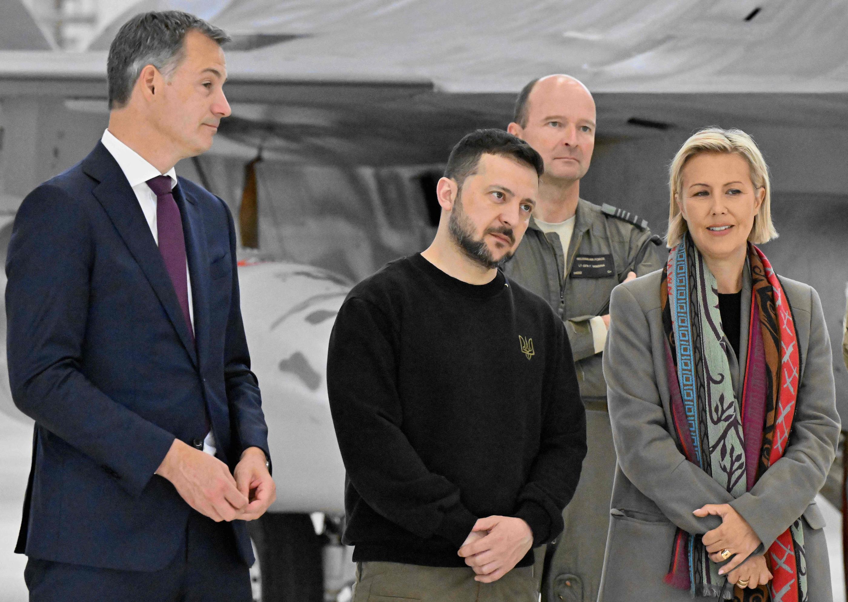 Le Premier ministre belge Alexander De Croo (à gauche), le président ukrainien Volodymyr Zelensky (au centre) et la ministre belge de la Défense Ludivine Dedonder (à droite) écoutent pilotes, instructeurs et techniciens belges de F-16  à l'aéroport militaire de Melsbroek. AFP/Belga/ERIC LALMAND.