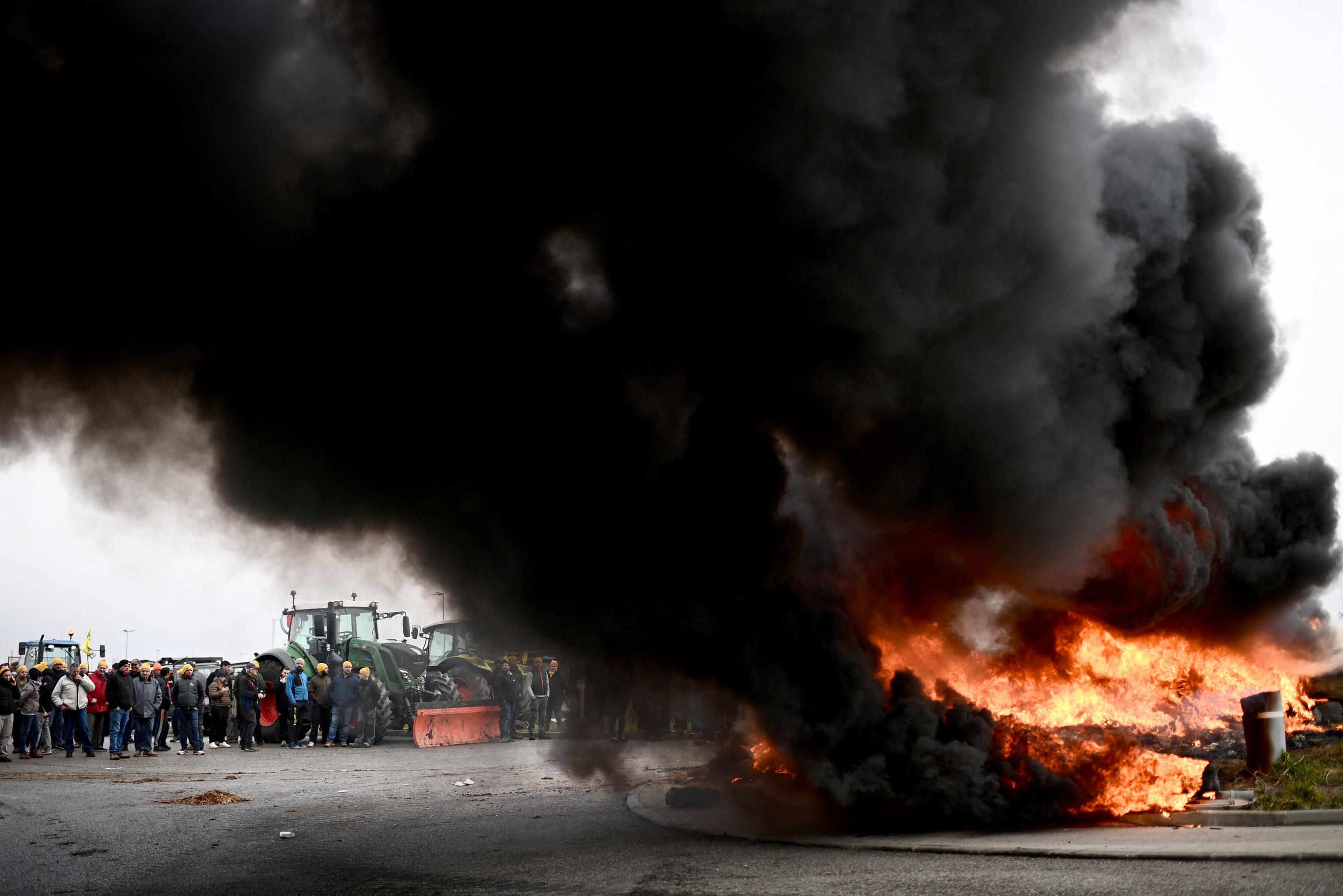 Des agriculteurs lot-et-garonnais brûlent des pneus et des branches devant un centre logistique Super U, près d'Agen, générant un immense nuage de fumée noire. AFP/Christophe Archambault