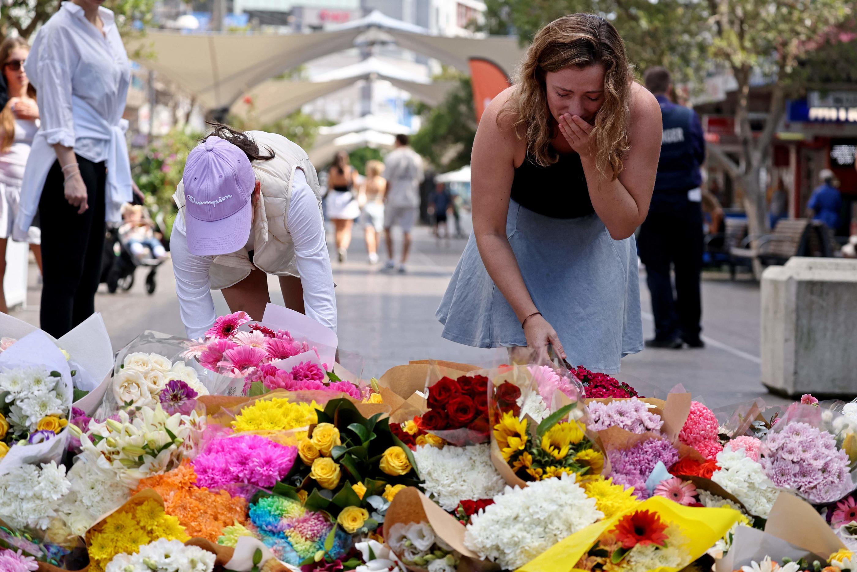 Des passants déposent des fleurs devant le centre commercial touché par une attaque meurtrière au couteau à Sydney, ce samedi. AFP/David Gray