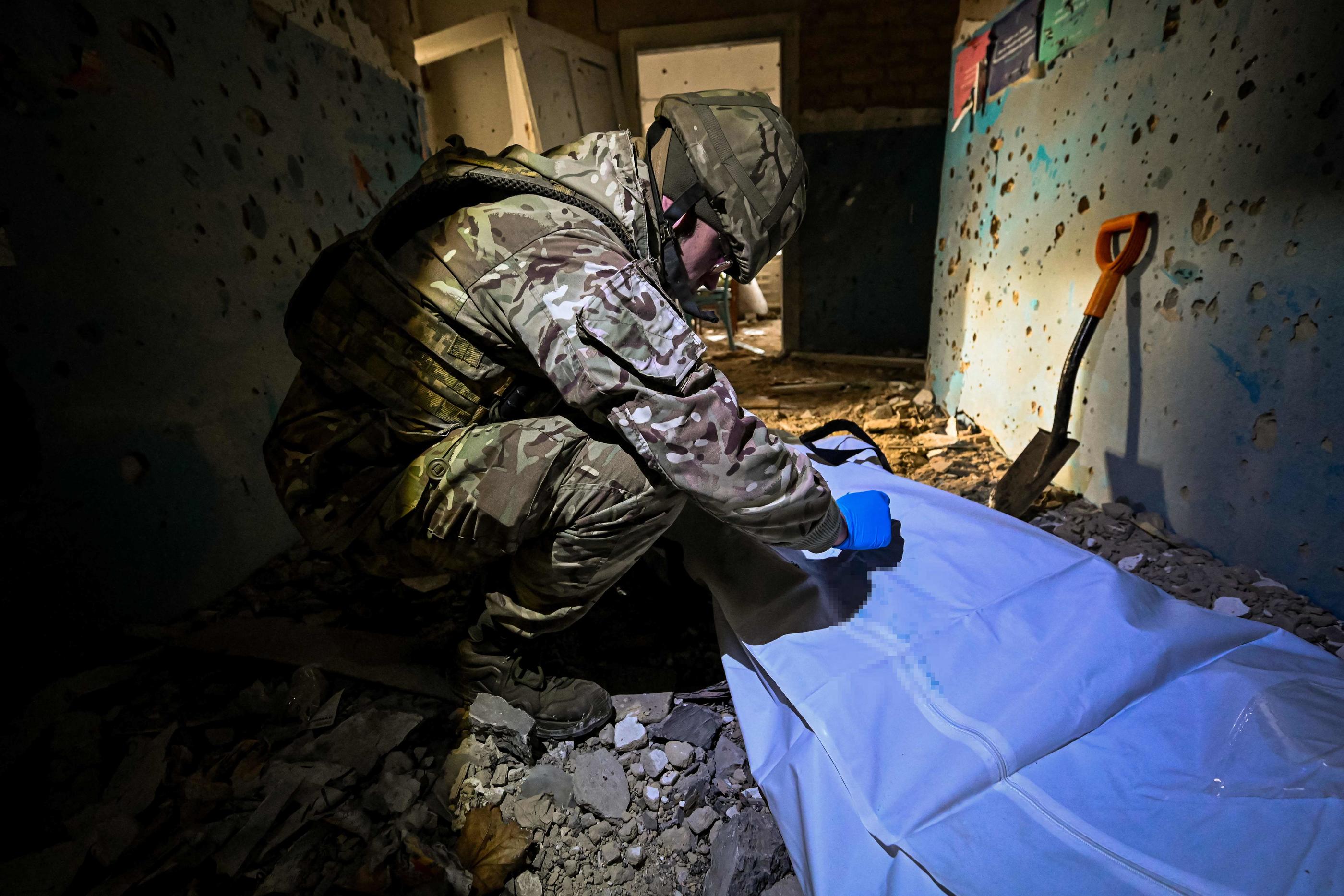 Un soldat ukrainien écrit le nom d'un soldat russe tué retrouvé dans un hôpital détruit lors de la libération du village de Petropavlivka, dans la région de Kharkiv, en décembre 2022. AFP /SERGEY BOBOK