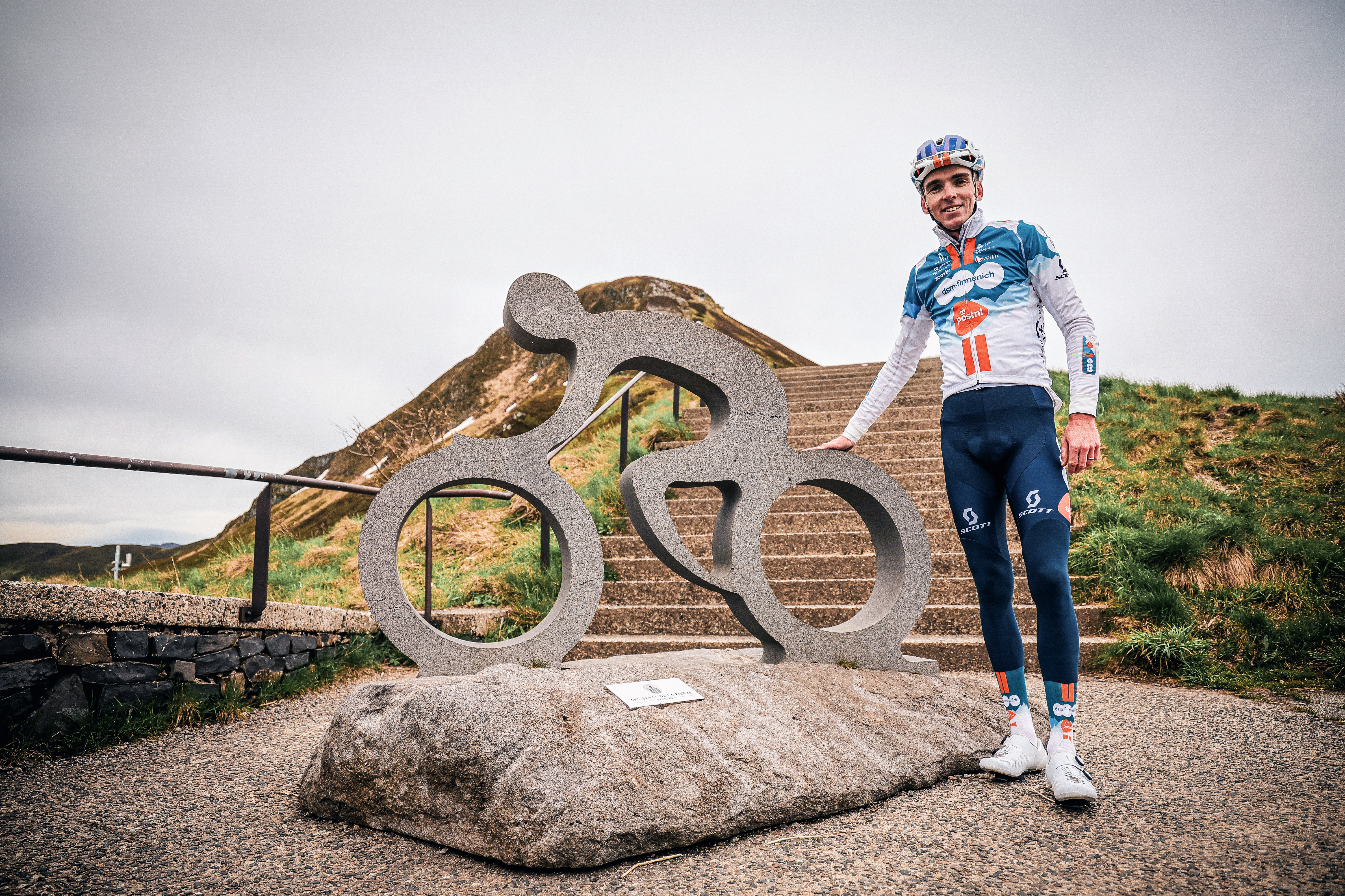 Au sommet du Pas de Peyrol (Cantal), Romain Bardet pose devant la sculpture en forme de vélo taillée dans de la pierre volcanique locale. DR