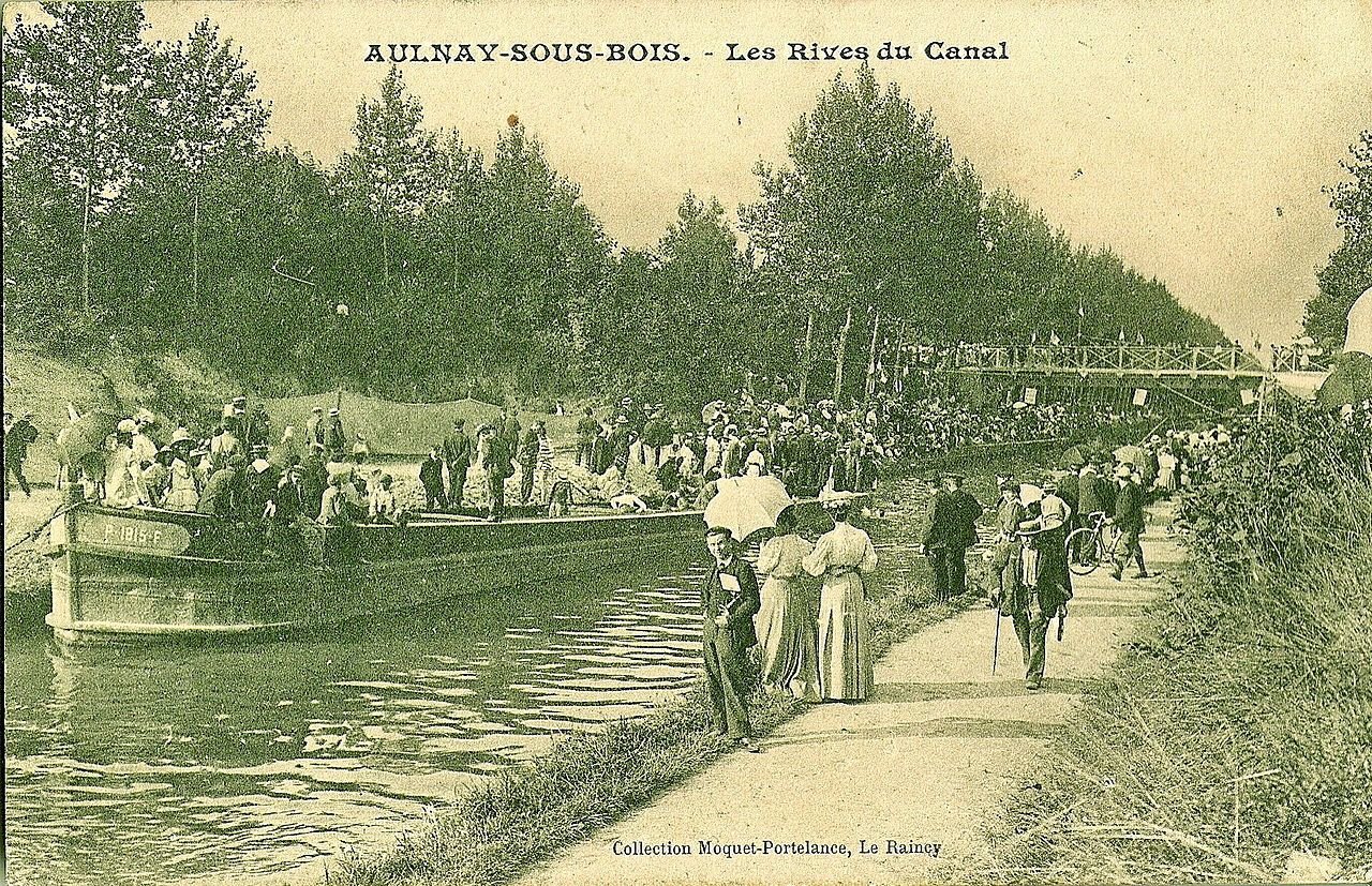 Carte postale en noir et blanc datée du début du XXe siècle figurant une scène de fête sur les bords du canal de l'Ourcq à Aulnay-sous-Bois. DR