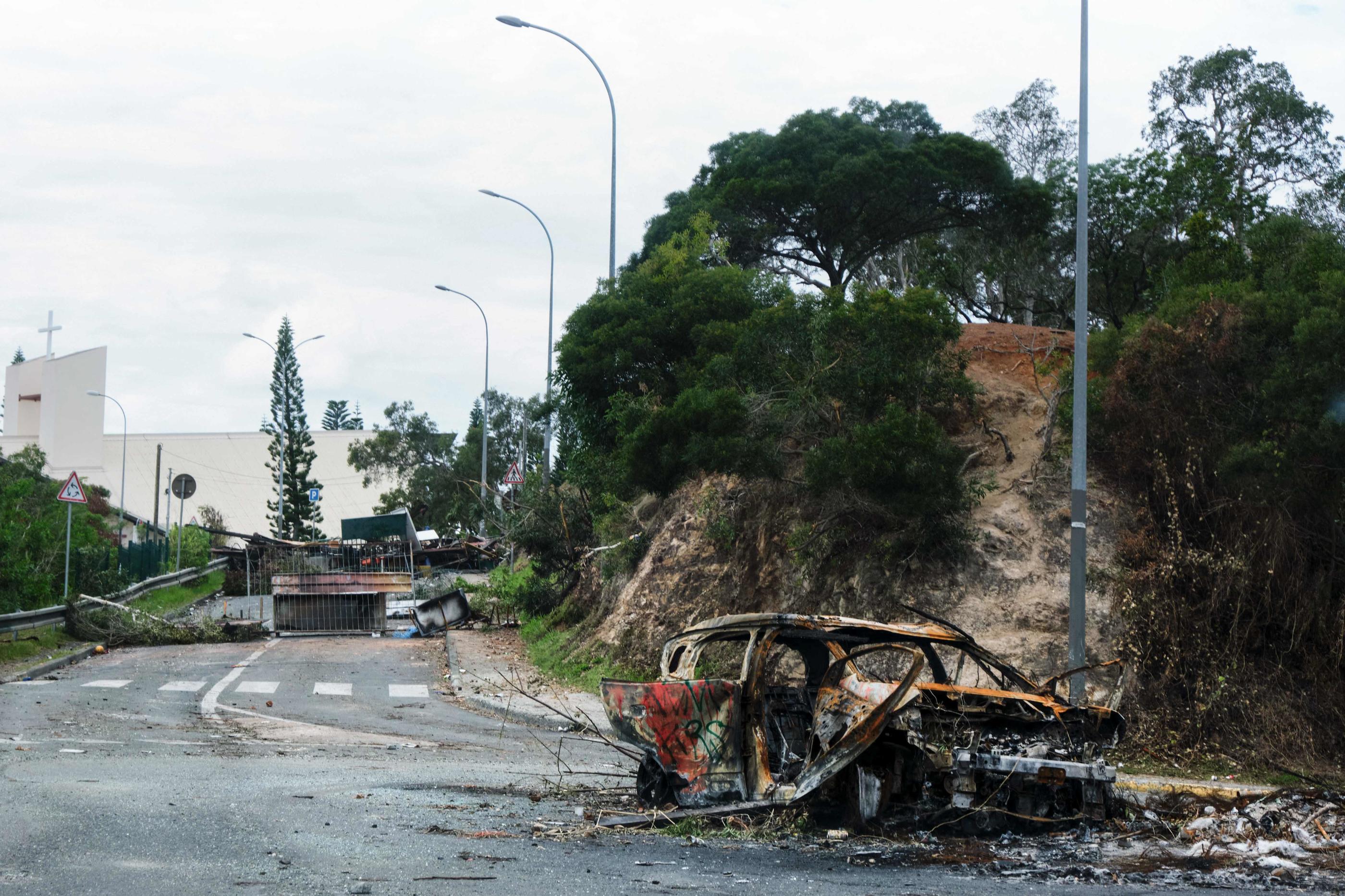 Un véhicule brûlé et des barrages sur une route près de la zone de Montravel à Nouméa, en Nouvelle-Calédonie, le 21 mai 2024. AFP/Théo Rouby