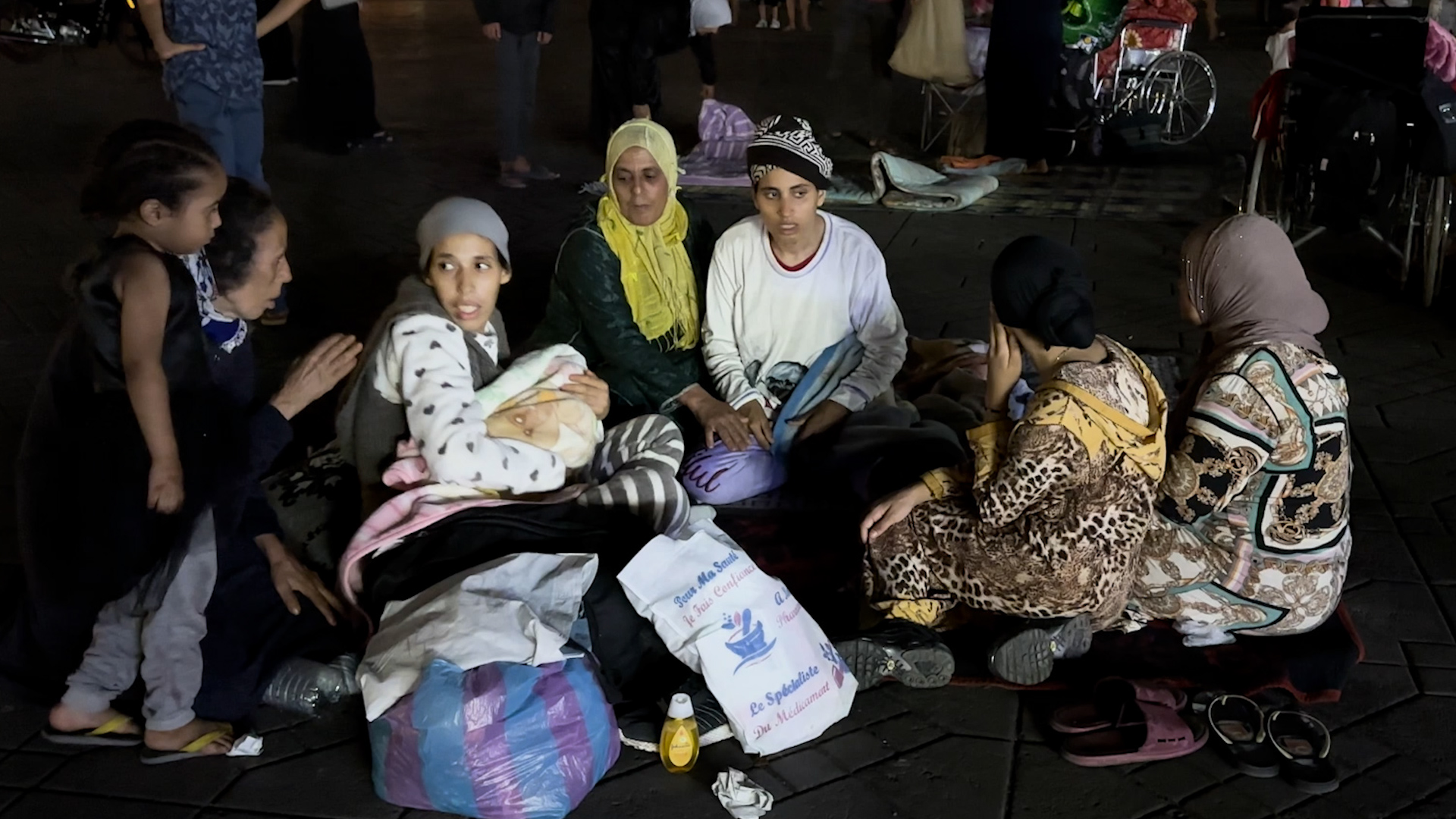 Marrakech, 9 septembre 2023.  Des petits groupes d’habitants du quartier de la médina se forment sur l’immense parvis, assis ou allongés sur des nattes et des couvertures.