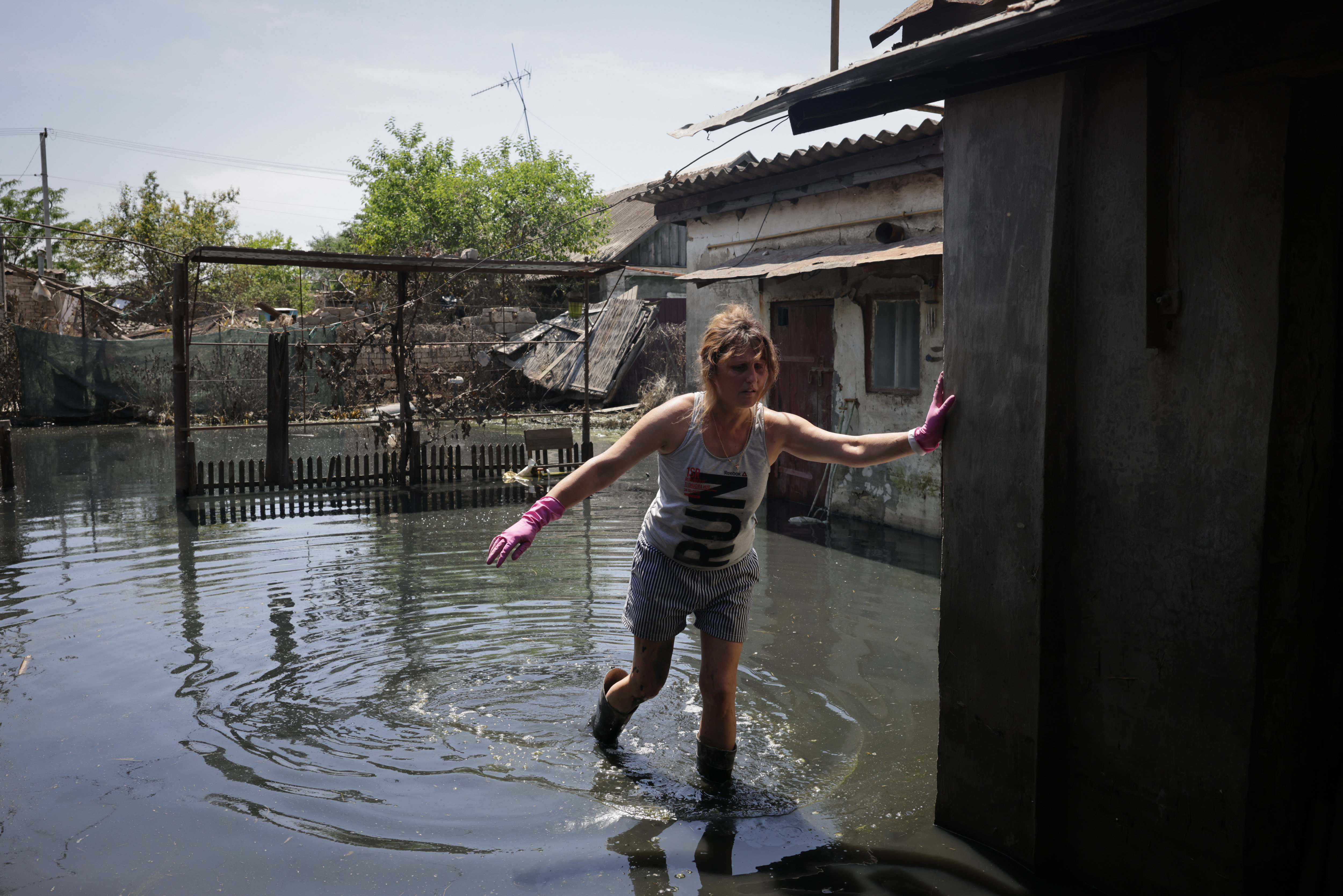 Kherson (Ukraine), le 20 juin 2023. Depuis deux jours, l'eau baisse et les habitants tentent de nettoyer ce qu'il reste de leur maison. Oksana, 48 ans, constate les dégâts. Il manque 20 cm à ses bottes en caoutchouc pour accéder au fond de son jardin.