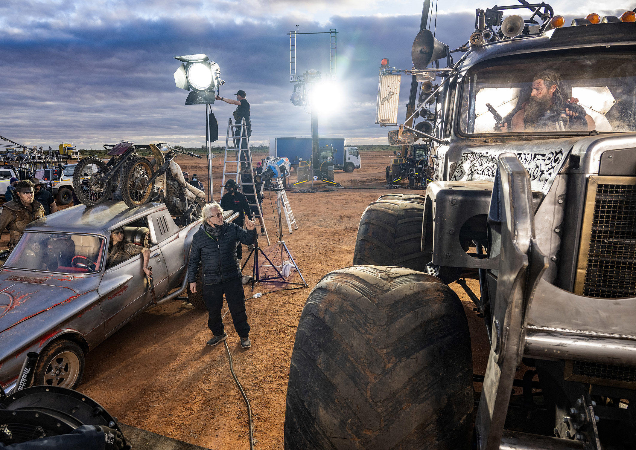 Le réalisateur George Miller (au centre) donnant des instructions sur le tournage de l'aventure «Furiosa» avec (de gauche à droite) Tom Burke, Anya Taylor-Joy (dans la voiture) et Chris Hemsworth (dans le camion). Warner Bros/Cr. Jasin Boland