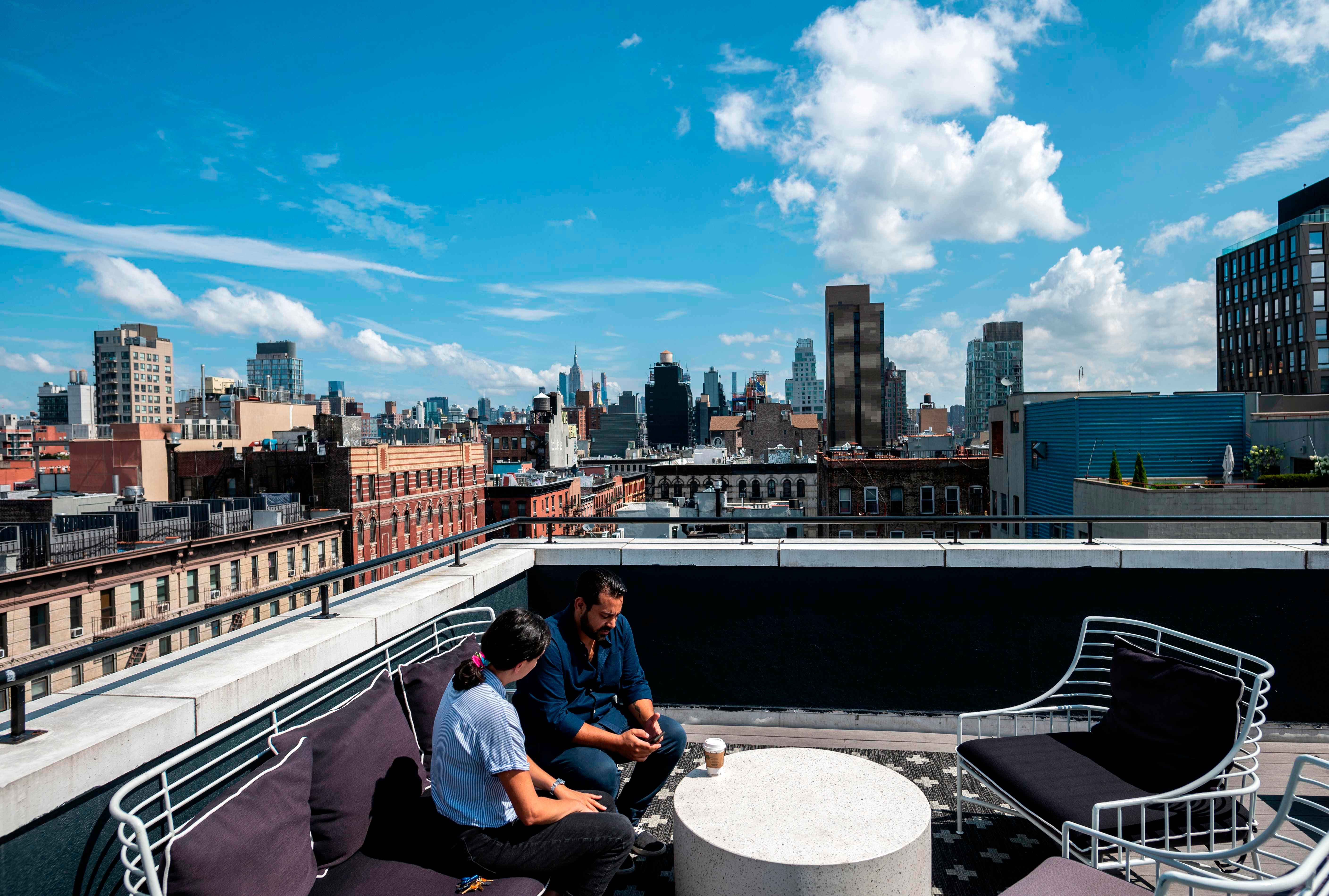 Gil Hirak (R), head of US operations and community of Quarters speaks with a colleague on the roof top of Quarters Co-Living in the Lower East Side on July 24, 2019 in New York City. - Nandita Iyer landed in New York from Bombay without knowing anyone, but she didn't want to live alone in a "sketchy studio." So instead she opted for a room in a "coliving" unit. She lives with roommates in one of the 14 apartments in a small building run by the housing start-up Quarters in the trendy Lower East Side neighborhood. The best part of the arrangement, she said, are the common areas: a large kitchen with a big table and comfy couches, a terrace where she can work and a luxurious rooftop patio. "I met people from such different backgrounds. And I became very good friends with them," she said. (Photo by Johannes EISELE / AFP)