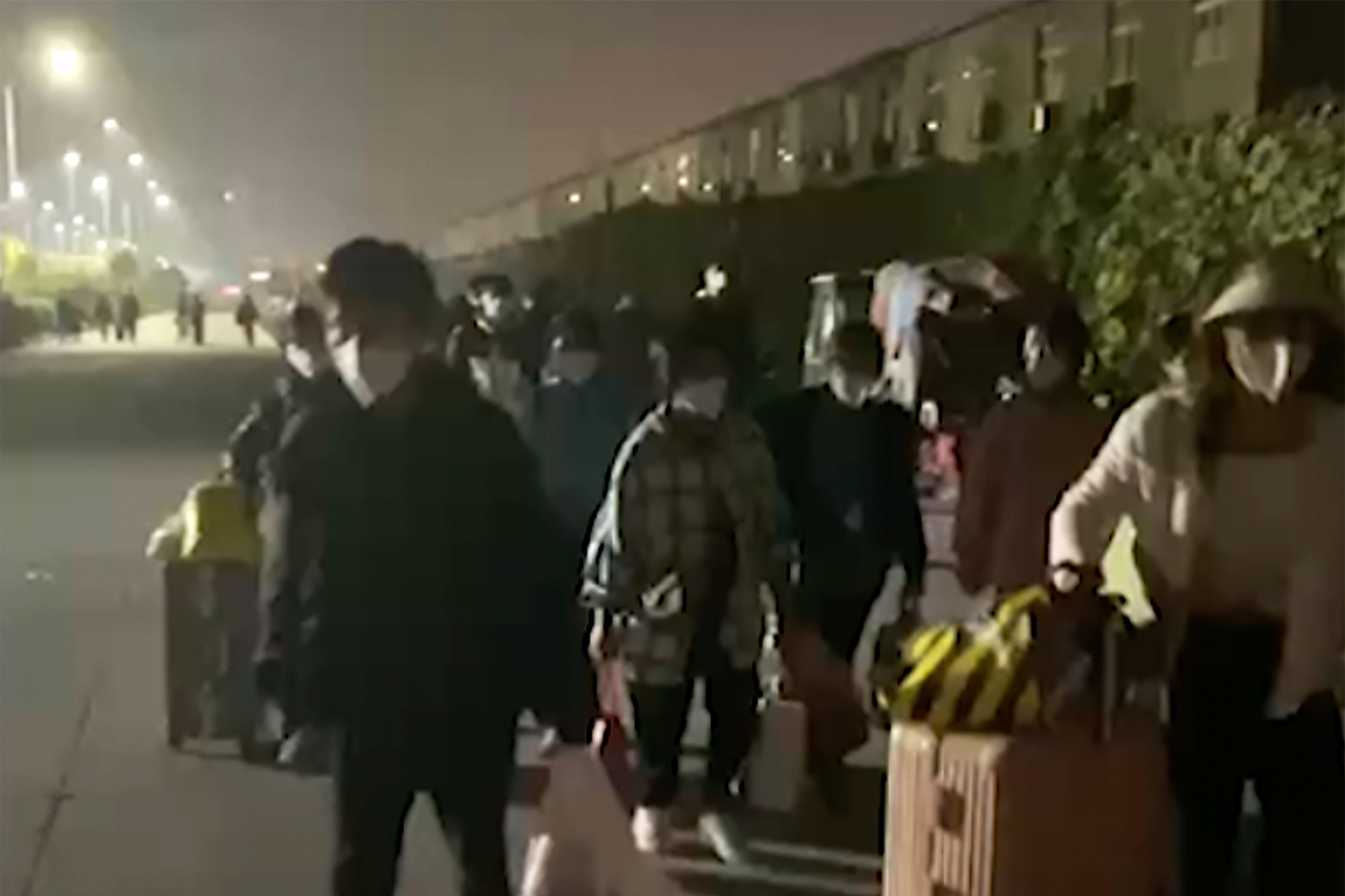 Bildet er av folk som har rømt fra en fabrikk og går langs en vei med kofferter og tepper. Foto: Hangpai Xingyang / AP / NTB