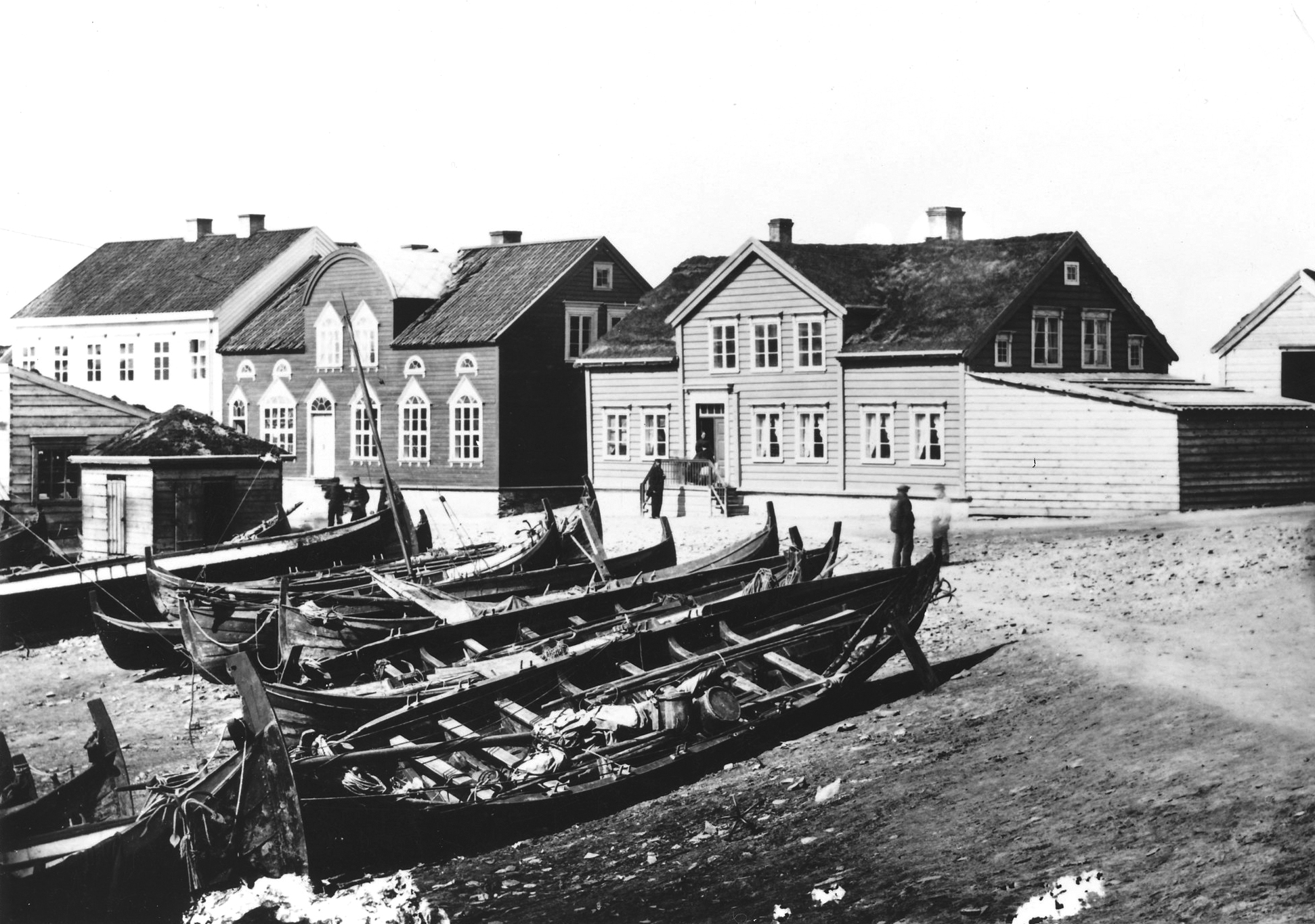 1865: Valen i Vardø frosset i tid: Fra venstre ser vi skolebygningen, kjøpmann Henrick Martin Borthens hus og kjøpmann Lauritz Odin Brodkorbs hus. Mannen og kvinnen som står henholdsvis foran og på trappen er trolig Lauritz Odin selv og hans kone Margrethe.