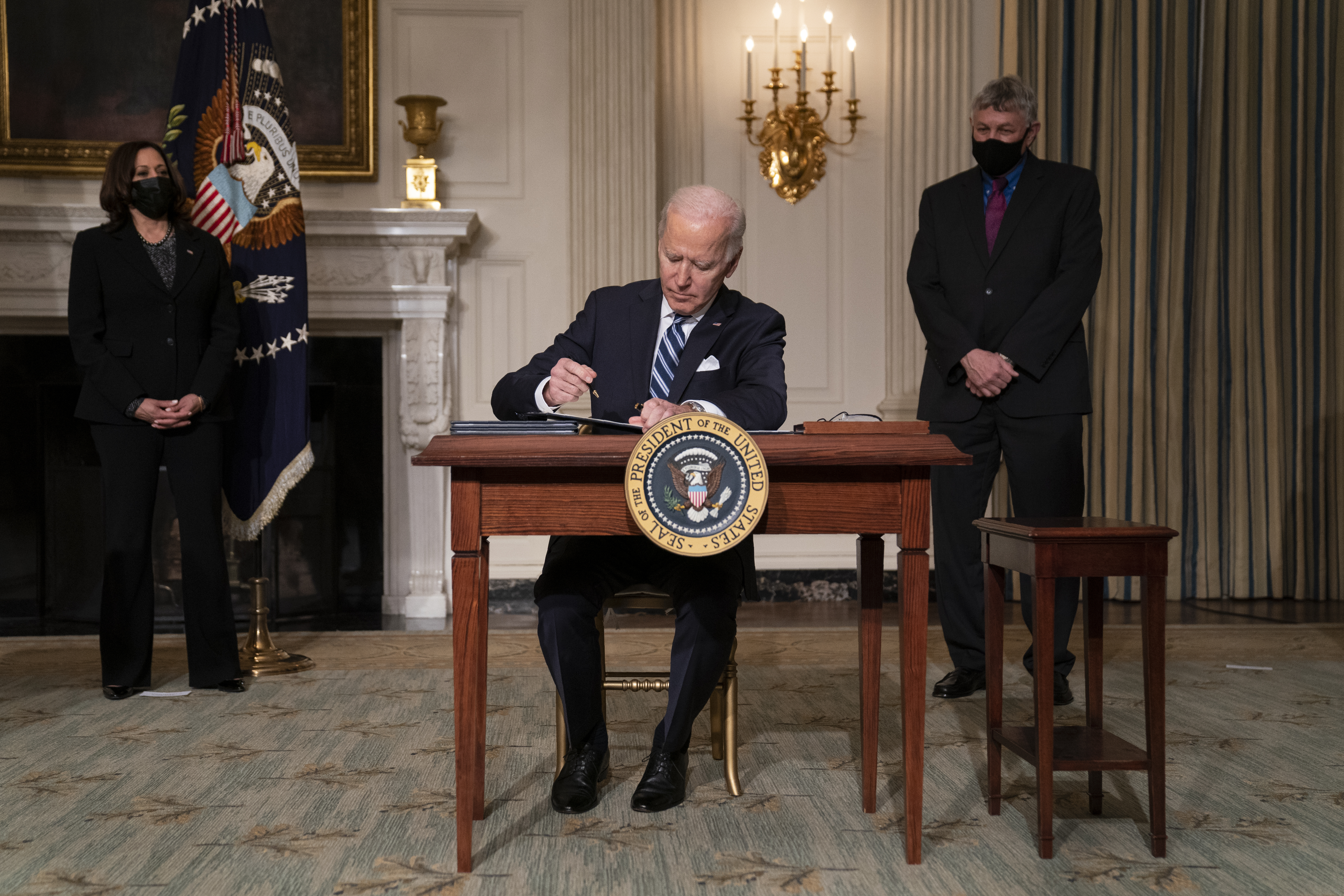Vice President Kamala Harris, left, and White House science adviser Dr. Eric Lander, right, look on as President Joe Biden signs a series of executive orders on climate change, in the State Dining Room of the White House, Wednesday, Jan. 27, 2021, in Washington. (AP Photo/Evan Vucci)