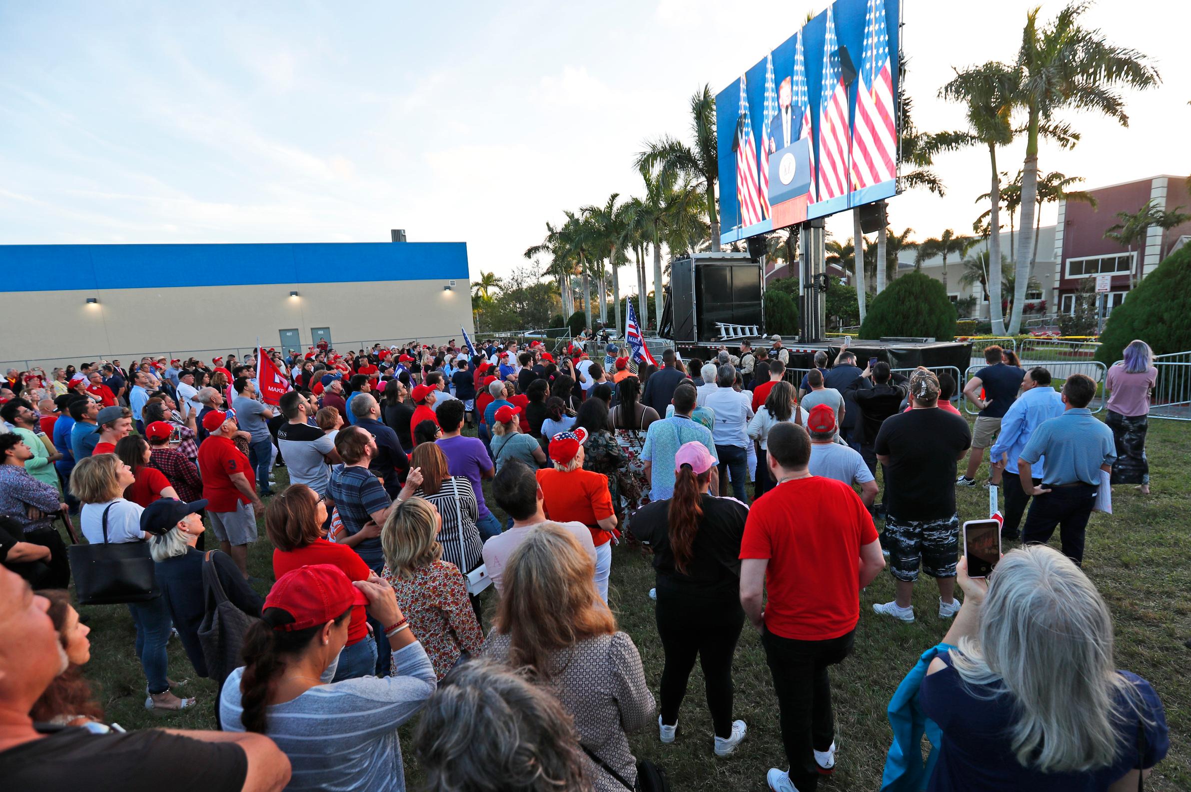 Attendees watch President Donald Trump on a large screen in an overflow area outside the King Jesus International Ministry, during a rally with the president, Friday, Jan. 3, 2020, in Miami. (AP Photo/Wilfredo Lee)