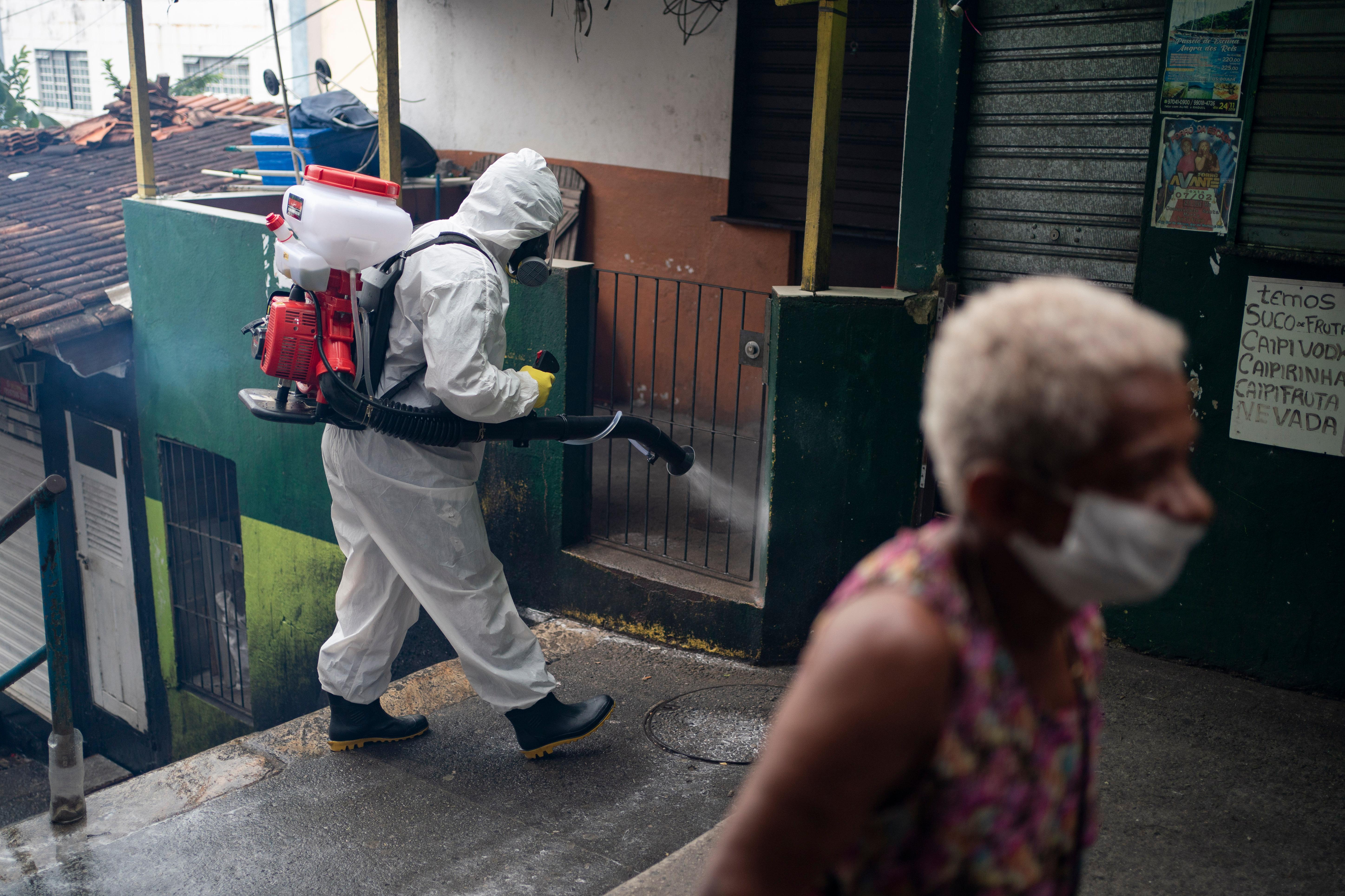 Thiago Firmino sprays disinfectant on an alley to avoid the spread the new corona virus at Santa Marta slum in Rio de Janeiro, Brazil, Friday, April 10, 2020. Firmino, who works as a tourist guide in the favela, helped organize a group to buy sanitization equipment with donated funds and are now disinfecting the alleyways of the favela. (AP Photo/Leo Correa)