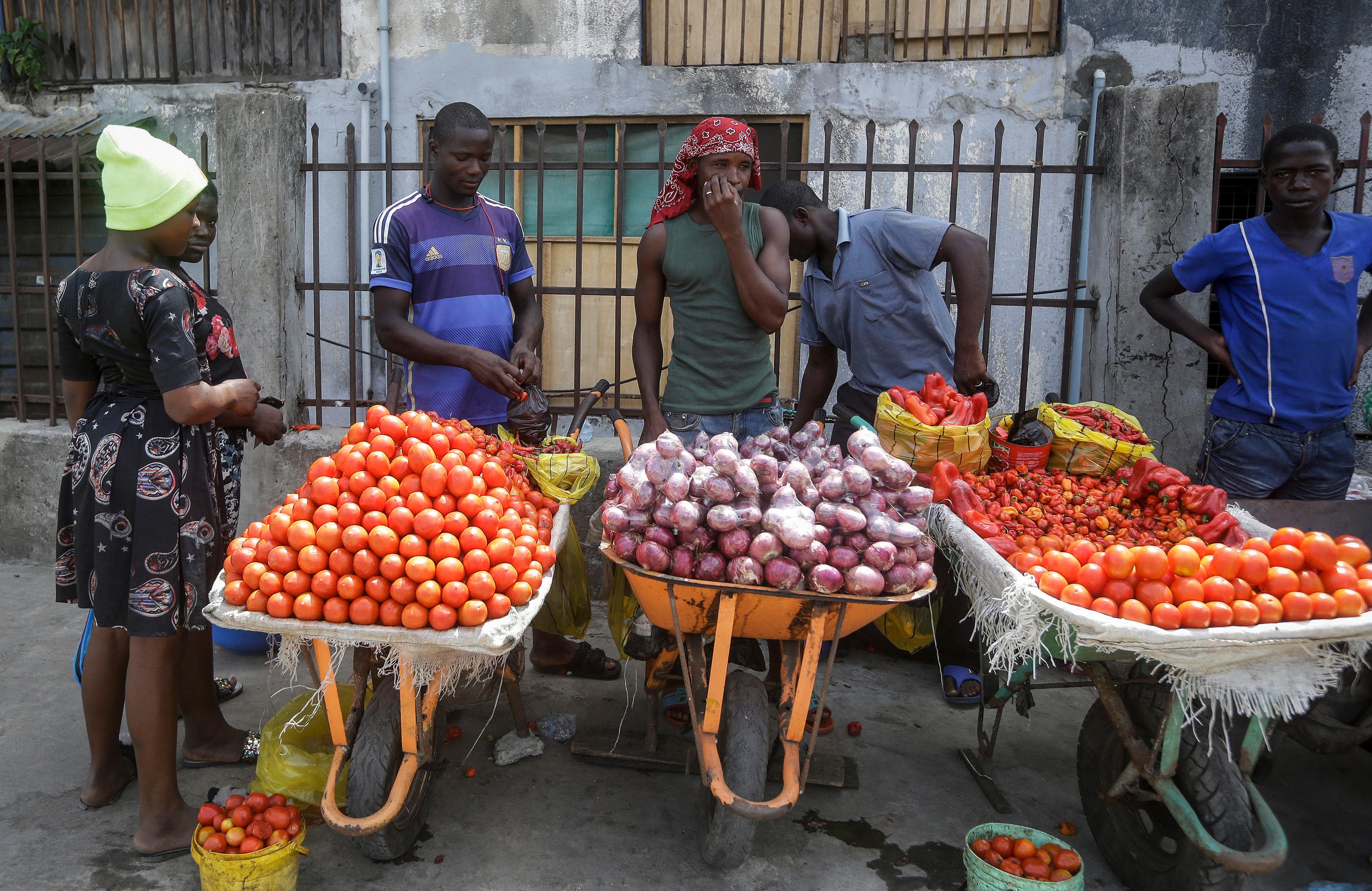 FILE - In this April 13, 2020, file photo, a woman buys tomatoes and onions from street sellers in Lagos, Nigeria. Lockdowns in Africa limiting the movement of people in an attempt to slow the spread of the coronavirus are threatening to choke off supplies of what the continent needs the most: Food. (AP Photo/Sunday Alamba, File)