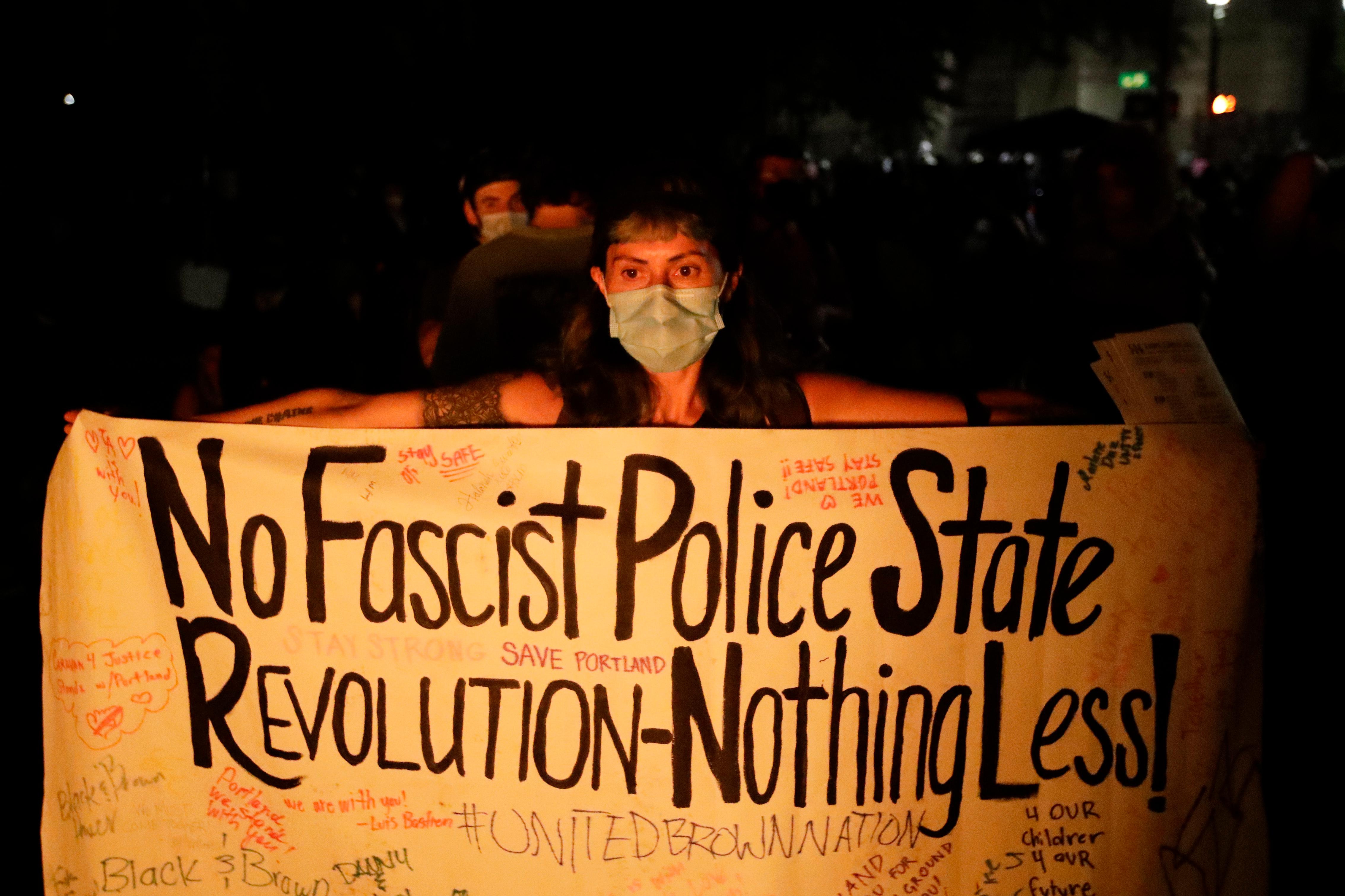 A demonstrator holds a sign in front of a fire during a Black Lives Matter protest at the Mark O. Hatfield United States Courthouse Tuesday, July 28, 2020, in Portland, Ore. (AP Photo/Marcio Jose Sanchez)