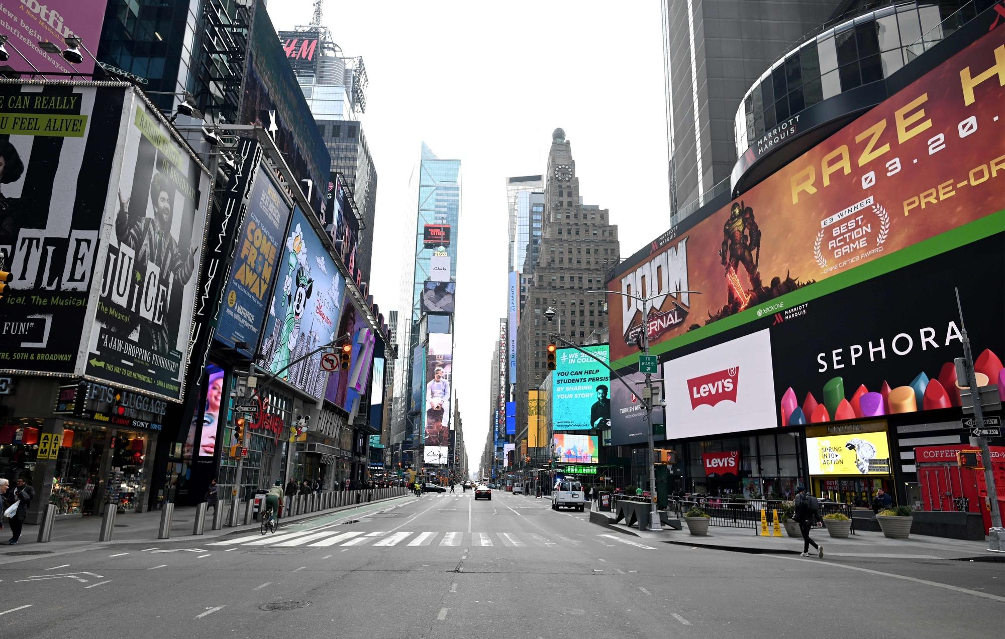 Few people are seen at Times Square in Manhattan on March 17, 2020 in New York City. - The coronavirus outbreak has transformed the US virtually overnight from a place of boundless consumerism to one suddenly constrained by nesting and social distancing.The crisis tests all retailers, leading to temporary store closures at companies like Apple and Nike, manic buying of food staples at supermarkets and big-box stores like Walmart even as many stores remain open for business -- albeit in a weirdly anemic consumer environment. (Photo by Johannes EISELE / AFP)