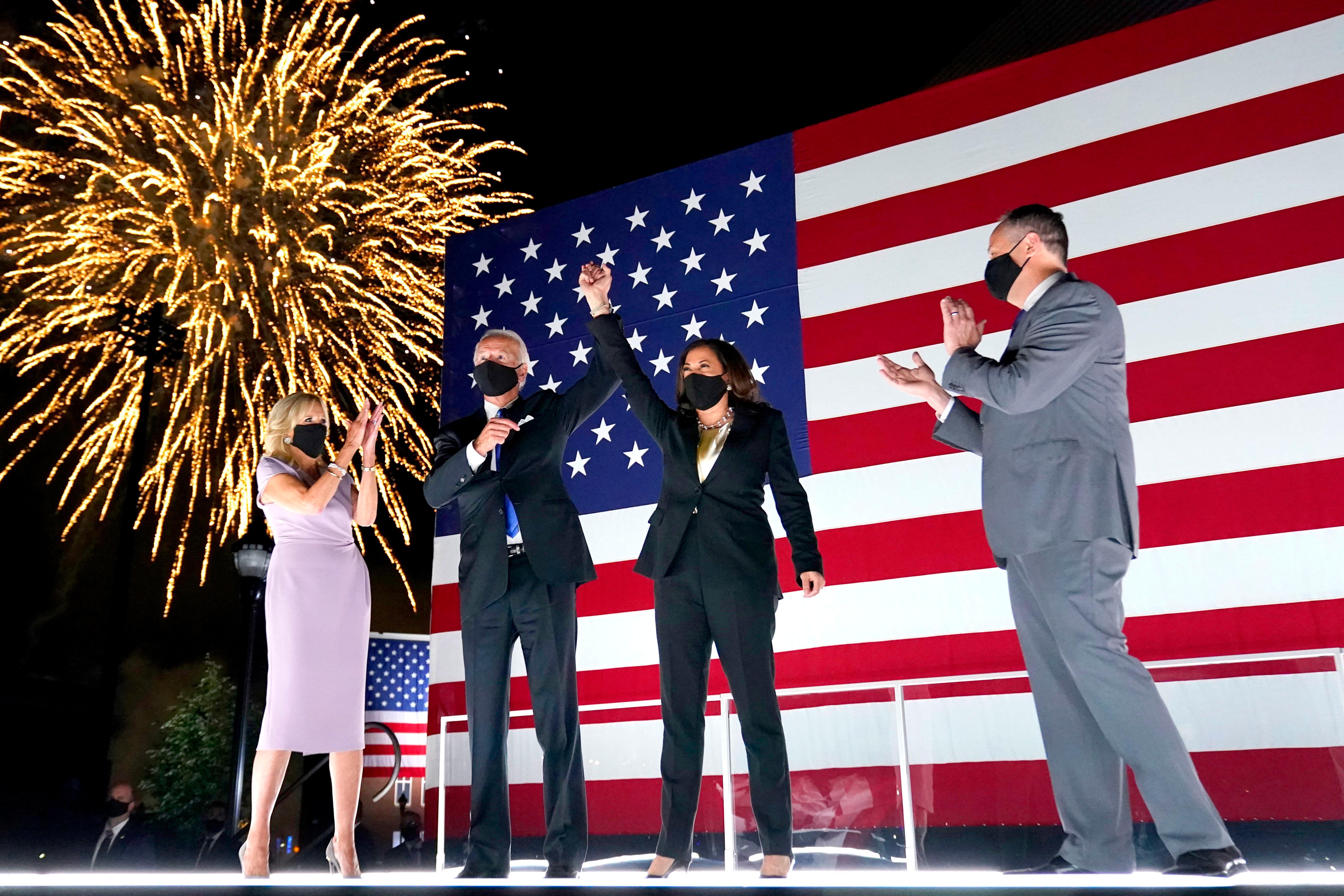 Democratic presidential candidate former Vice President Joe Biden, with Democratic vice presidential candidate Sen. Kamala Harris, D-Calif., raise their arms up as fireworks go off in the background during the fourth day of the Democratic National Convention, Thursday, Aug. 20, 2020, at the Chase Center in Wilmington, Del. Looking on are Jill Biden, far left, and Harris' husband Doug Emhoff, far right. (AP Photo/Andrew Harnik)