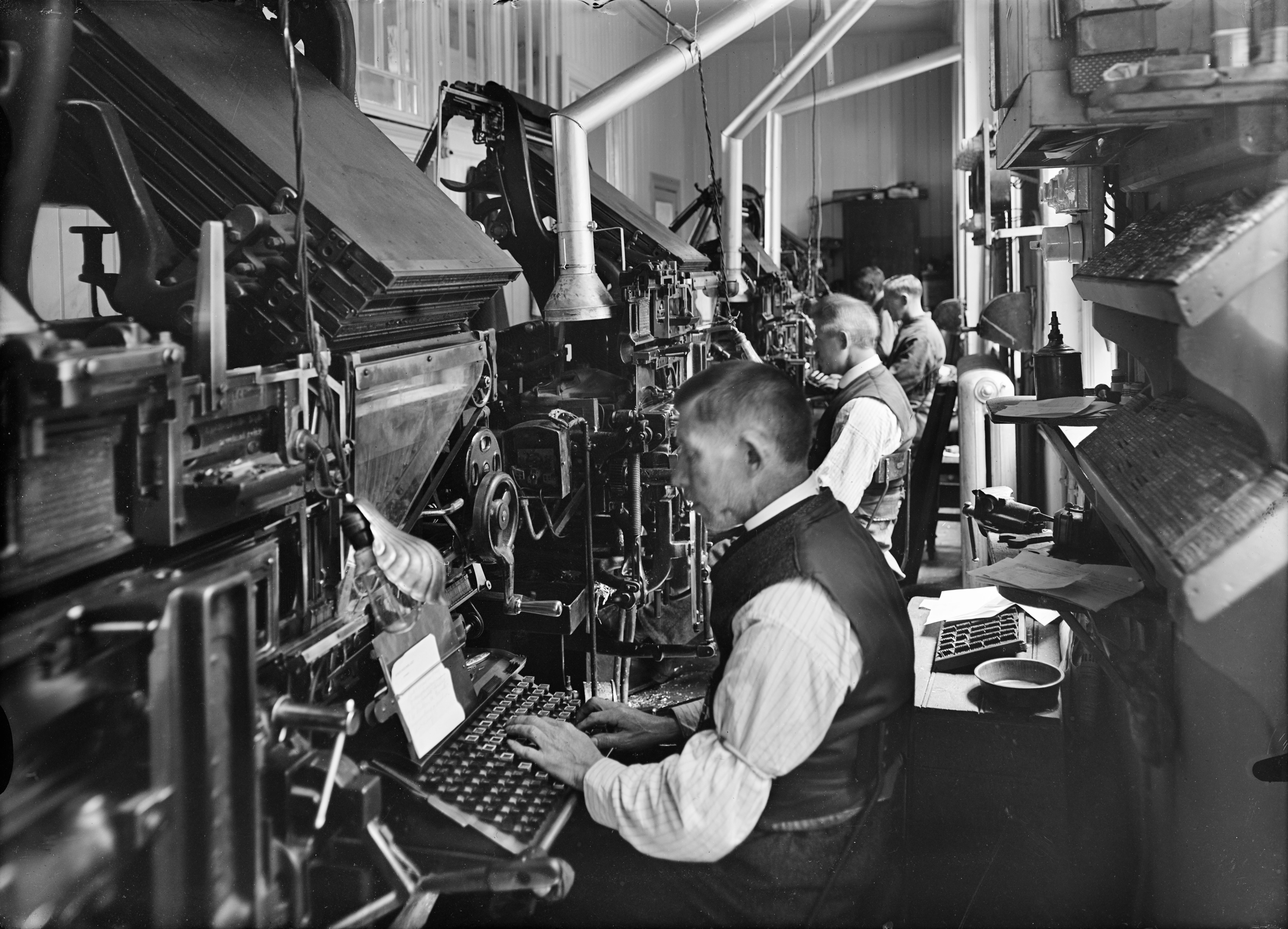 Settemaskiner ble utvikla allerede på 1820-tallet, men kom for alvor i bruk med Linotype-maskina fra 1886. Da fikk typografene mindre befatning med blystøv og farge, og kunne dermed ha hvite skjorter som arbeidsantrekk – «hvitsnipparbeidere». Foto fra Emil Moestue trykkeri i Norbygata 12 i 1938.