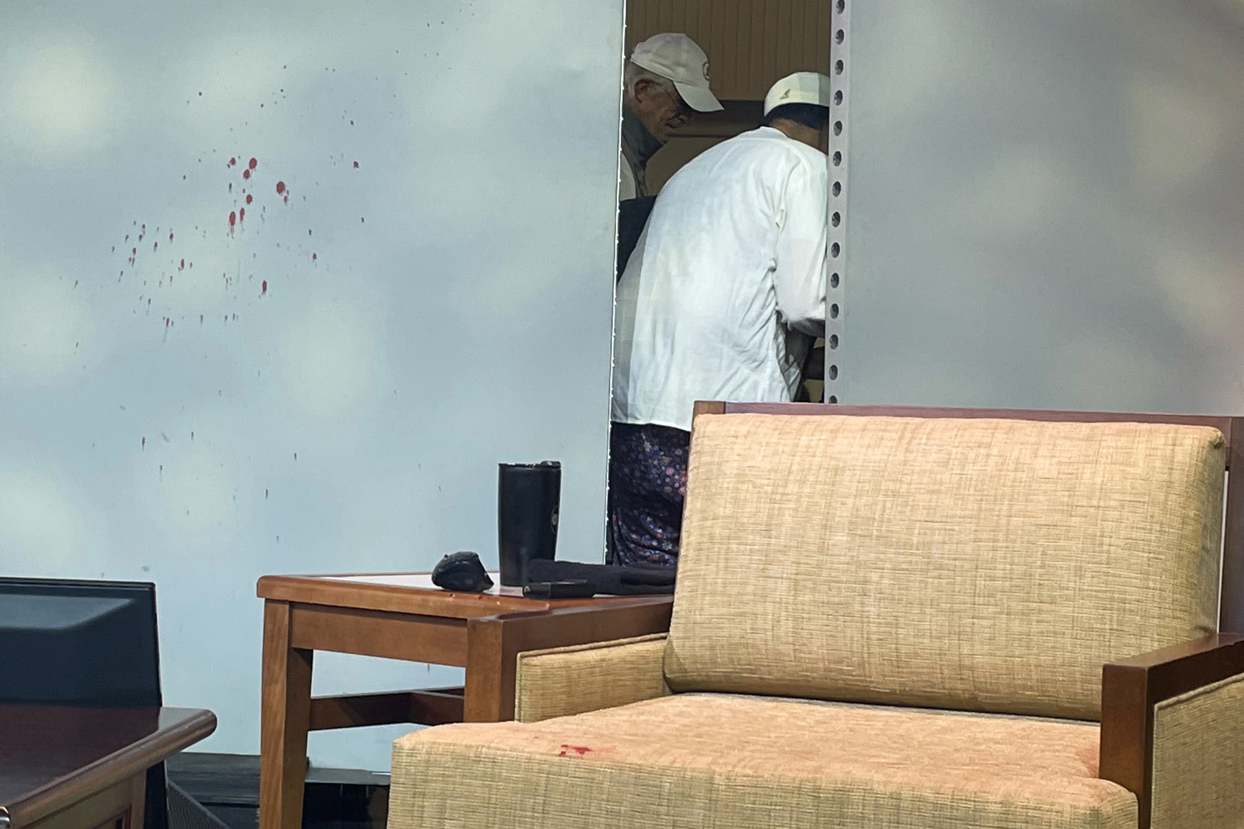 Blood stains mark a screen as author Salman Rushdie, behind screen, is tended to after he was attacked during a lecture, Friday, Aug. 12, 2022, at the Chautauqua Institution in Chautauqua, N.Y. (AP Photo/Joshua Goodman)