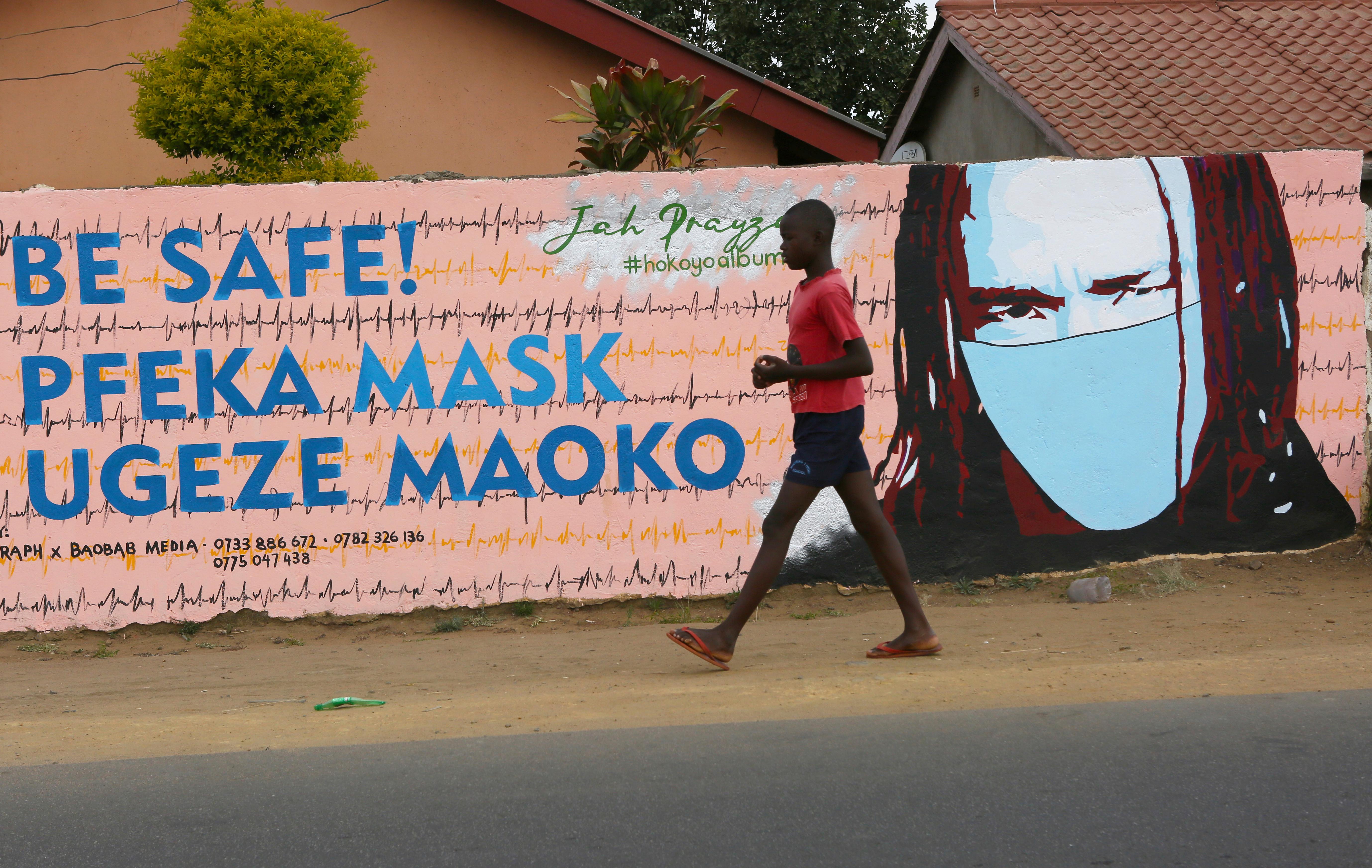 A young boy walks past a wall with graffiti urging people to wear face masks in Harare, Thursday, May, 28, 2020. Manhunts have begun after hundreds of people, some with the coronavirus, fled quarantine centres in Zimbabwe and Malawi while authorities worry they will spread COVID-19 in countries whose health systems can be rapidly overwhelmed. (AP Photo/Tsvangirayi Mukwazhi)