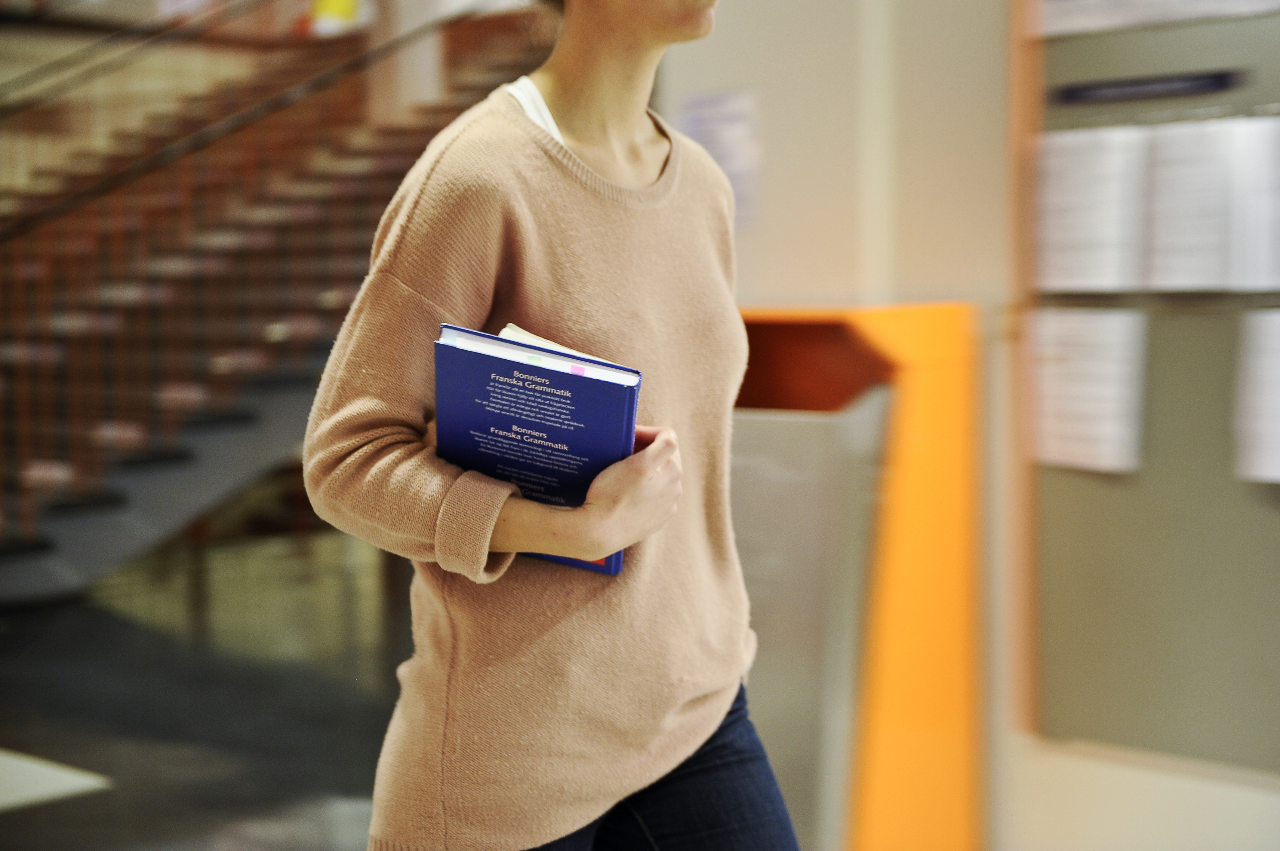 Kvinnlig student går i skolkorridor med böcker.