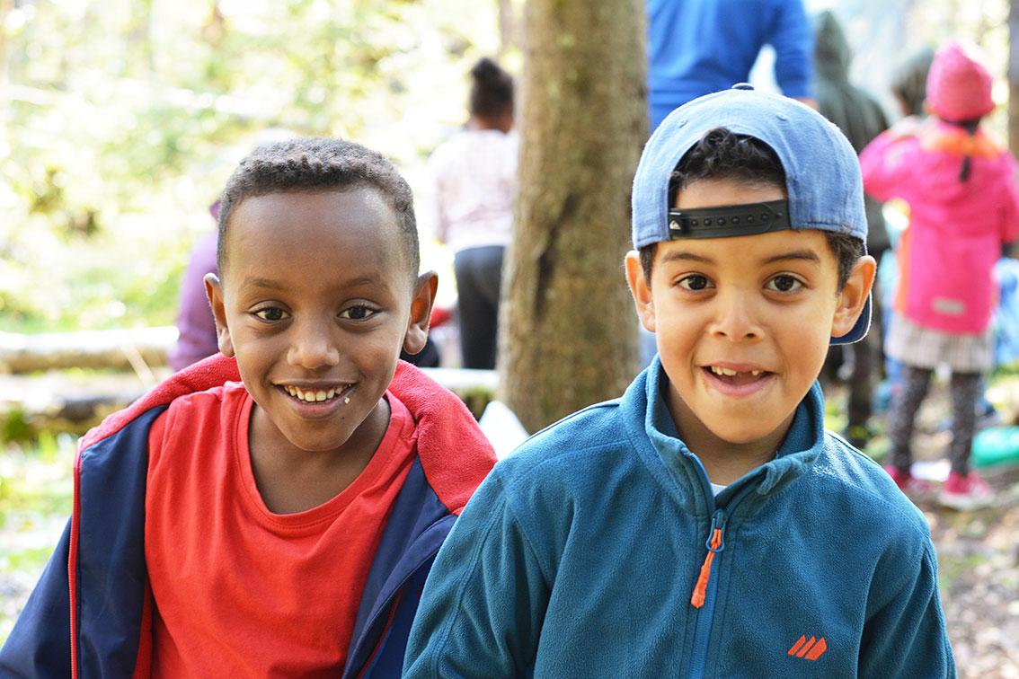 Bildet viser elevene Jaasiel og Mohamed som smiler. De trives med skole ute i det fri.