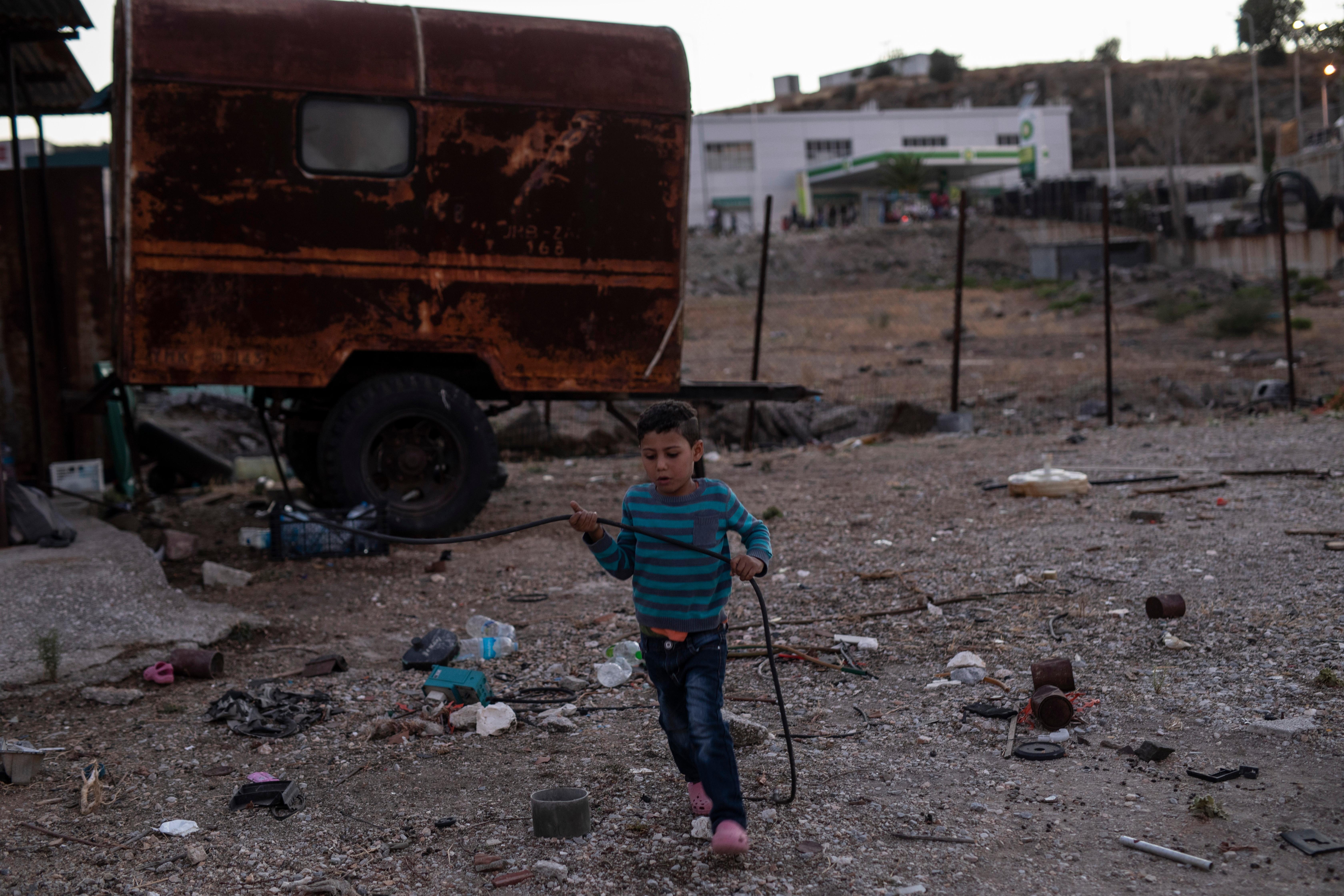 A migrant boy plays next to an abandoned vehicle on the northeastern island of Lesbos, Greece, Thursday, Sept. 10, 2020. Little remained of Greece's notoriously overcrowded Moria refugee camp Thursday after a second fire overnight destroyed nearly everything that had been spared in the original blaze, leaving thousands more people in need of emergency housing. (AP Photo/Petros Giannakouris)