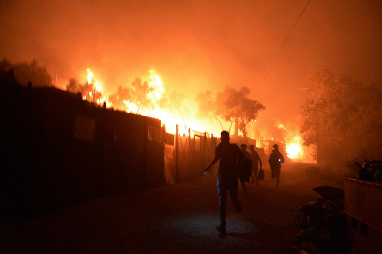 Refugees and migrants run as fire burns in the Moria refugee camp on the northeastern Aegean island of Lesbos, Greece, on Wednesday, Sept. 9, 2020. Fire Service officials say a large refugee camp on the Greek island of Lesbos has been partially evacuated despite a COVID-19 lockdown after fires broke out at multiple points around the site early Wednesday. (AP Photo/Panagiotis Balaskas)